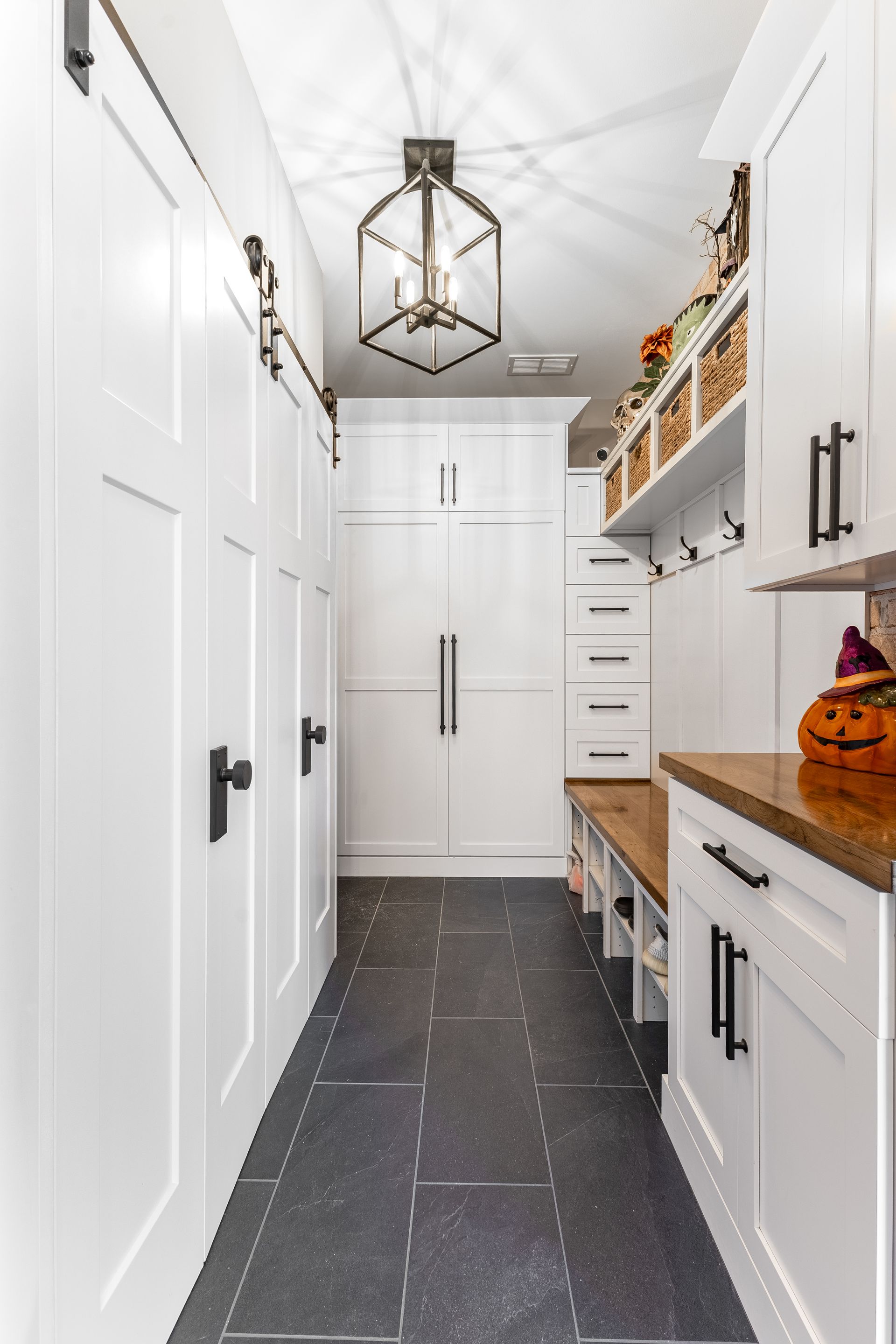 Narrow, white-walled hallway with dark floor, cabinets, and a hanging light fixture.