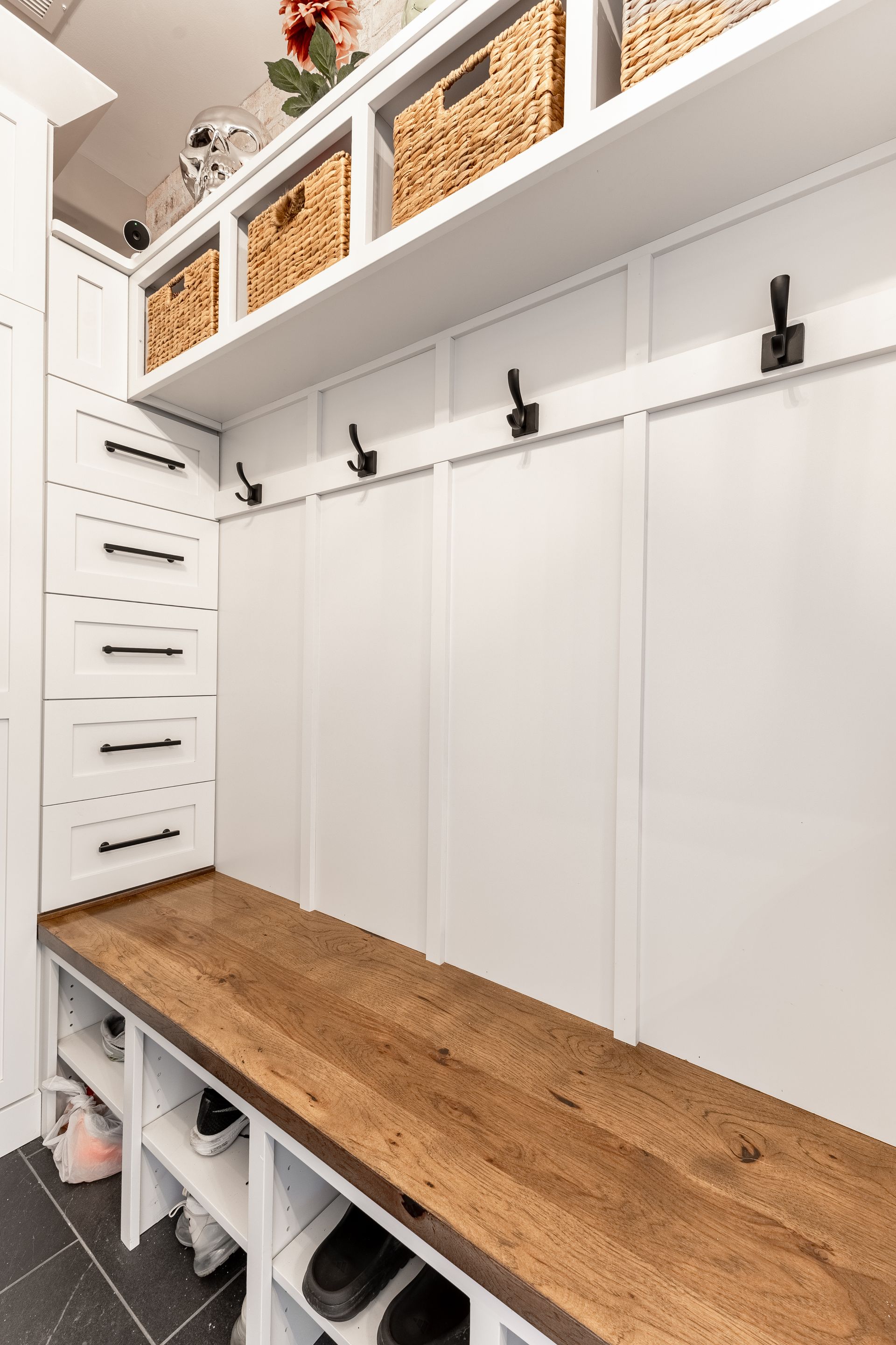 White built-in mudroom with a wood bench, storage baskets, hooks, and shoe cubbies.