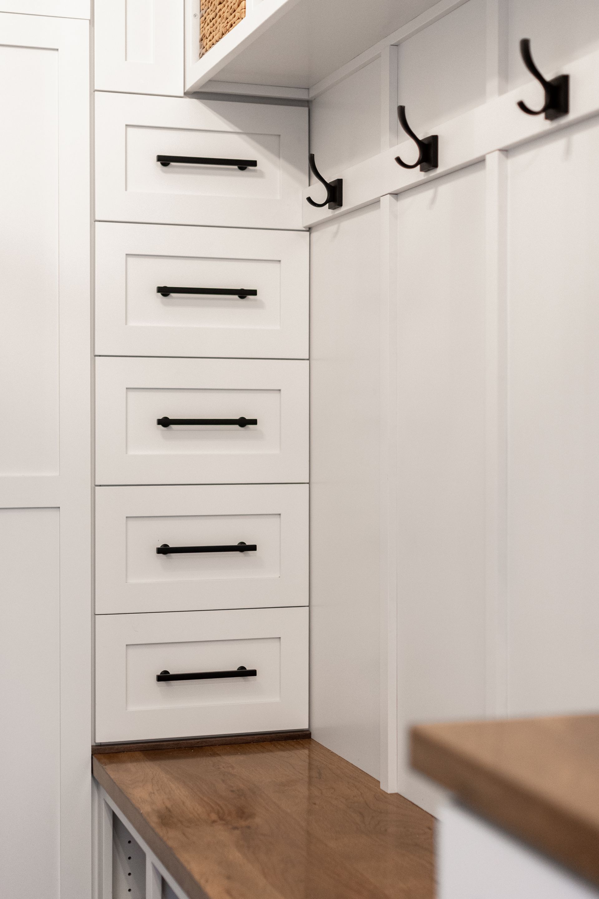 White storage cabinets with black handles and hooks. Wooden countertop.