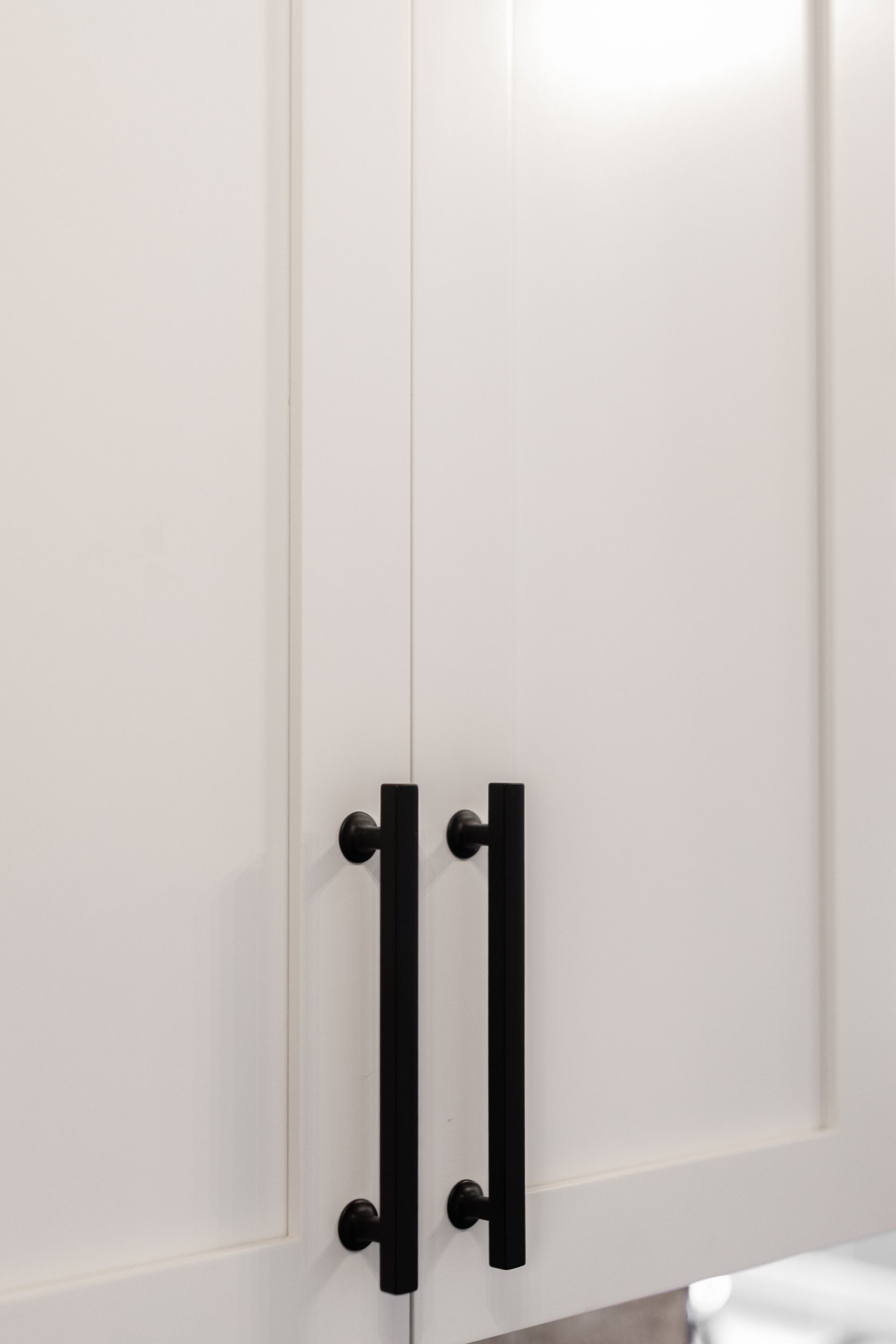 White kitchen cabinet doors with black bar handles.