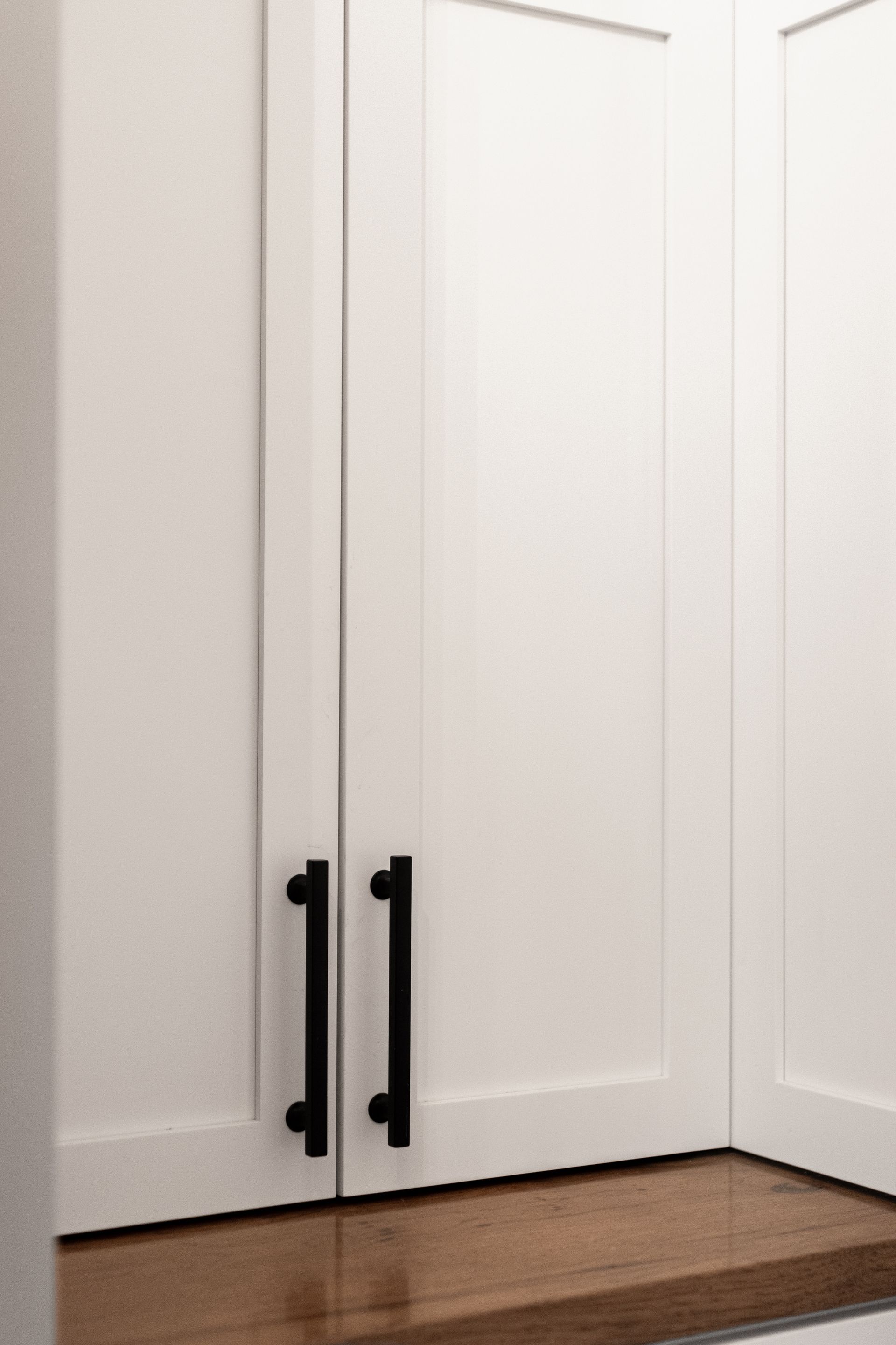 White cabinet doors with black handles, set in a corner over a wooden countertop.