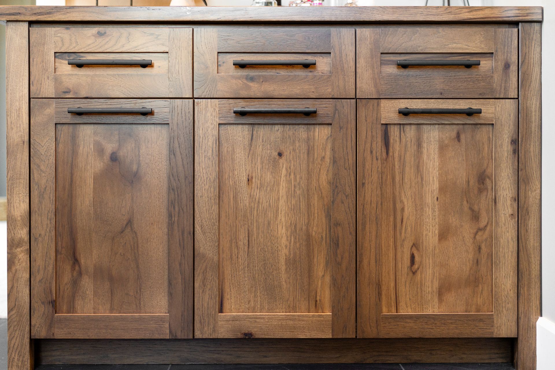 Wooden bathroom cabinet with three drawers and two doors, dark stain with black handles.