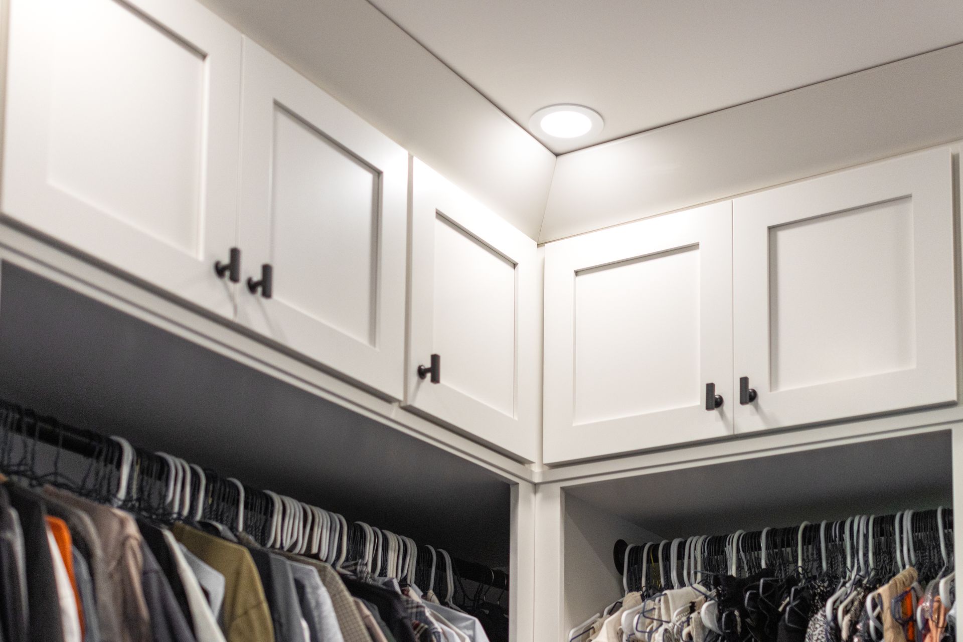 White closet cabinets with black handles, clothes hanging below.