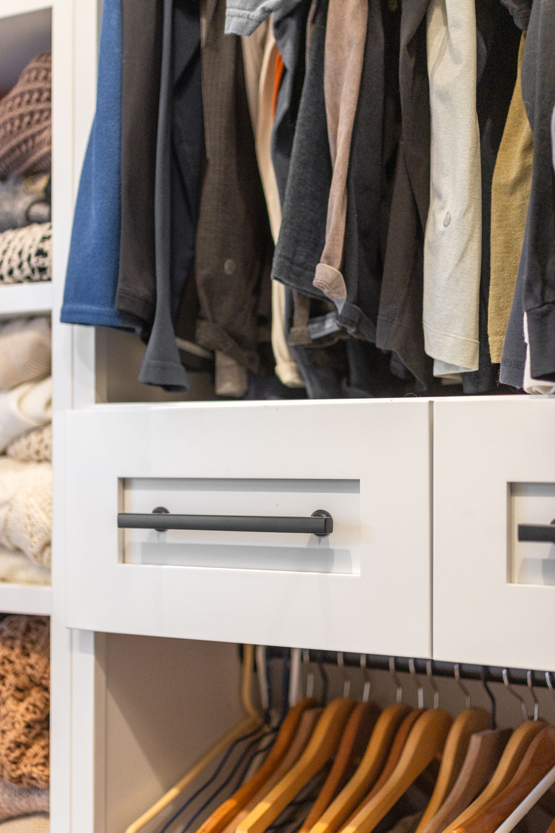 White closet drawers with black bar handles. Clothes hang above and below.