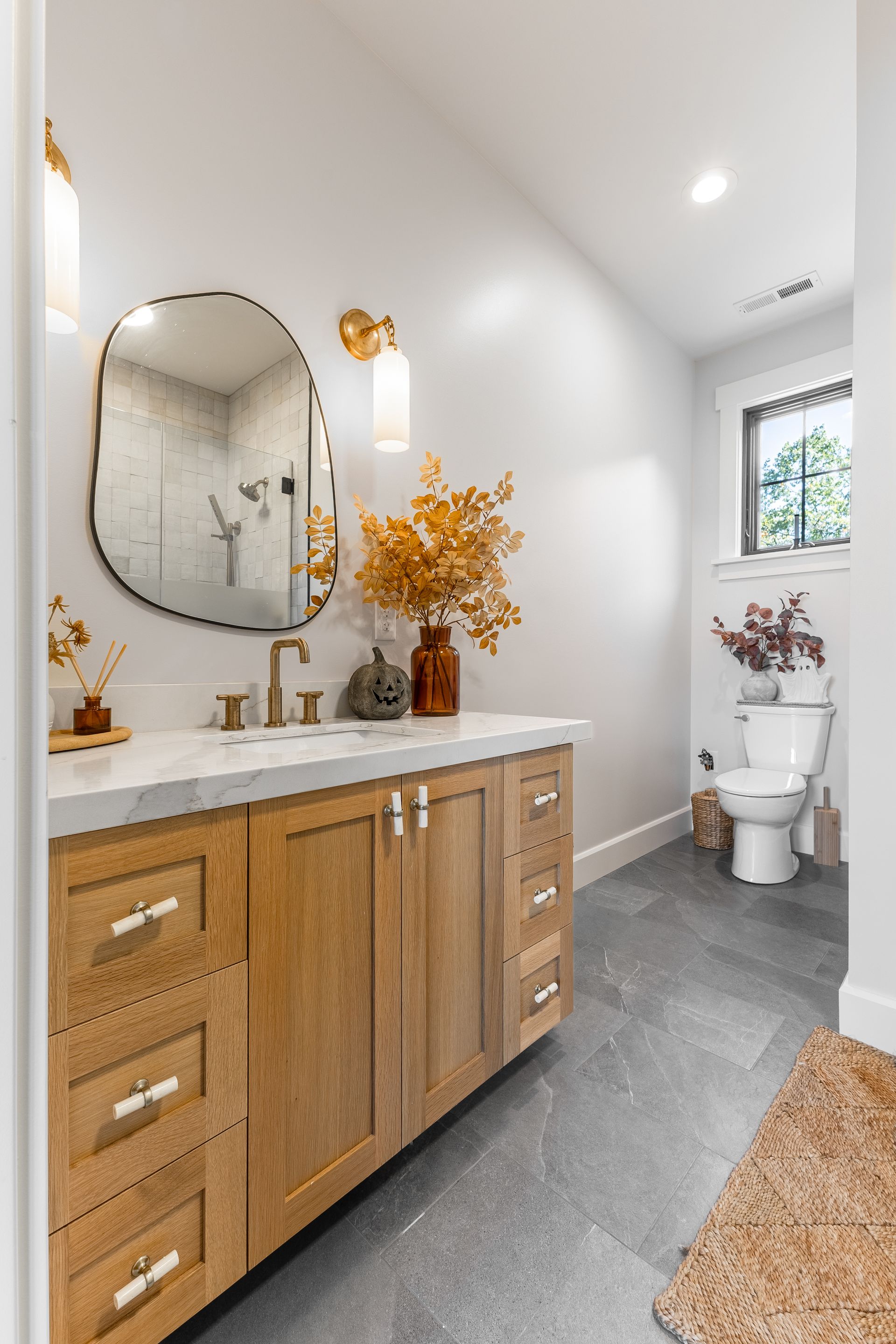 Bathroom with wood vanity, irregular mirror, and neutral-toned decor.