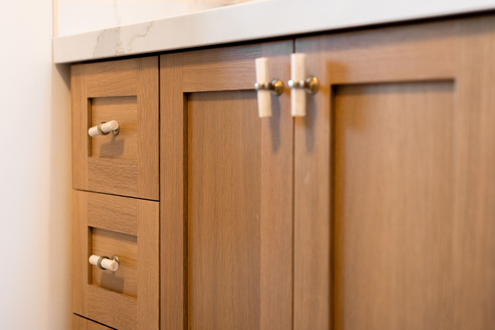 Wooden bathroom vanity with cabinet doors and drawers. Gold and white knobs.