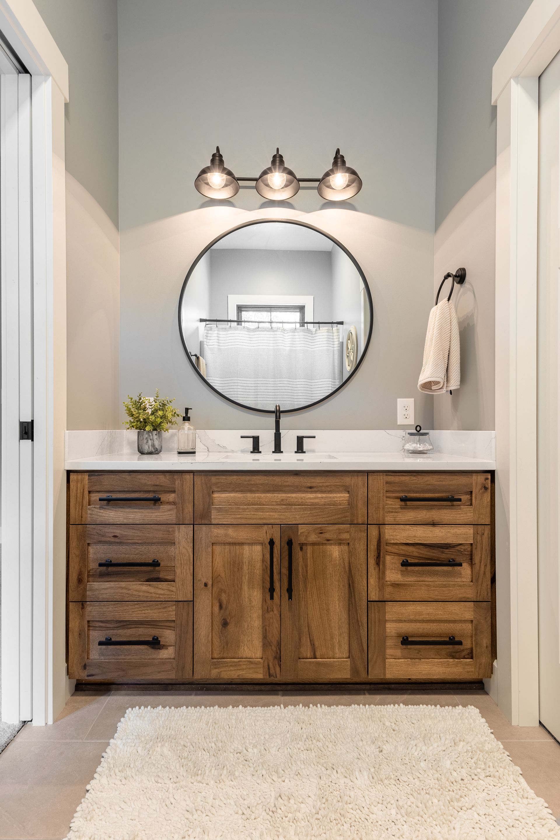 Rustic bathroom with a wooden vanity, round mirror, and a fluffy white rug.