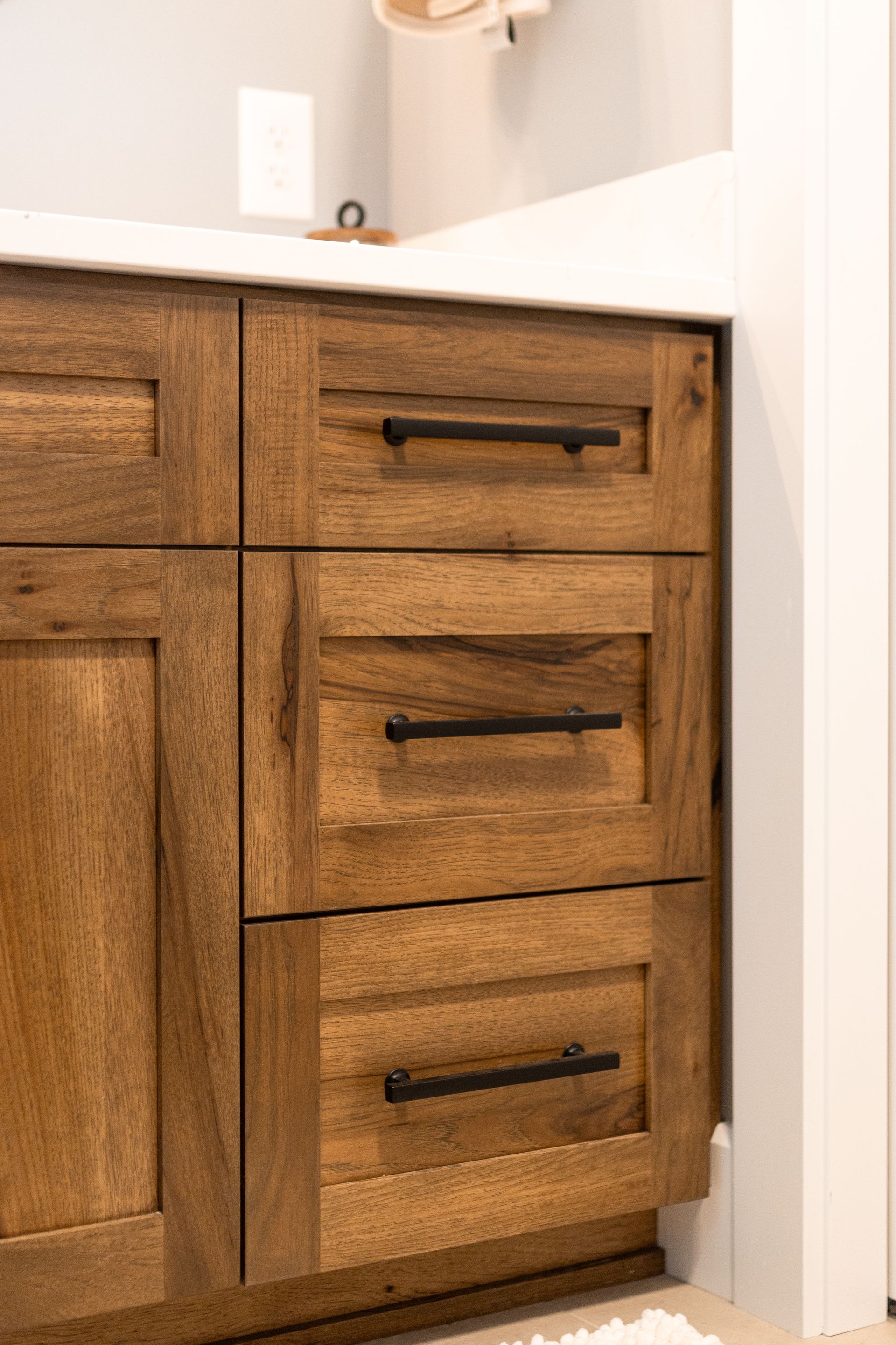 Wooden bathroom vanity with black handles and white countertop.