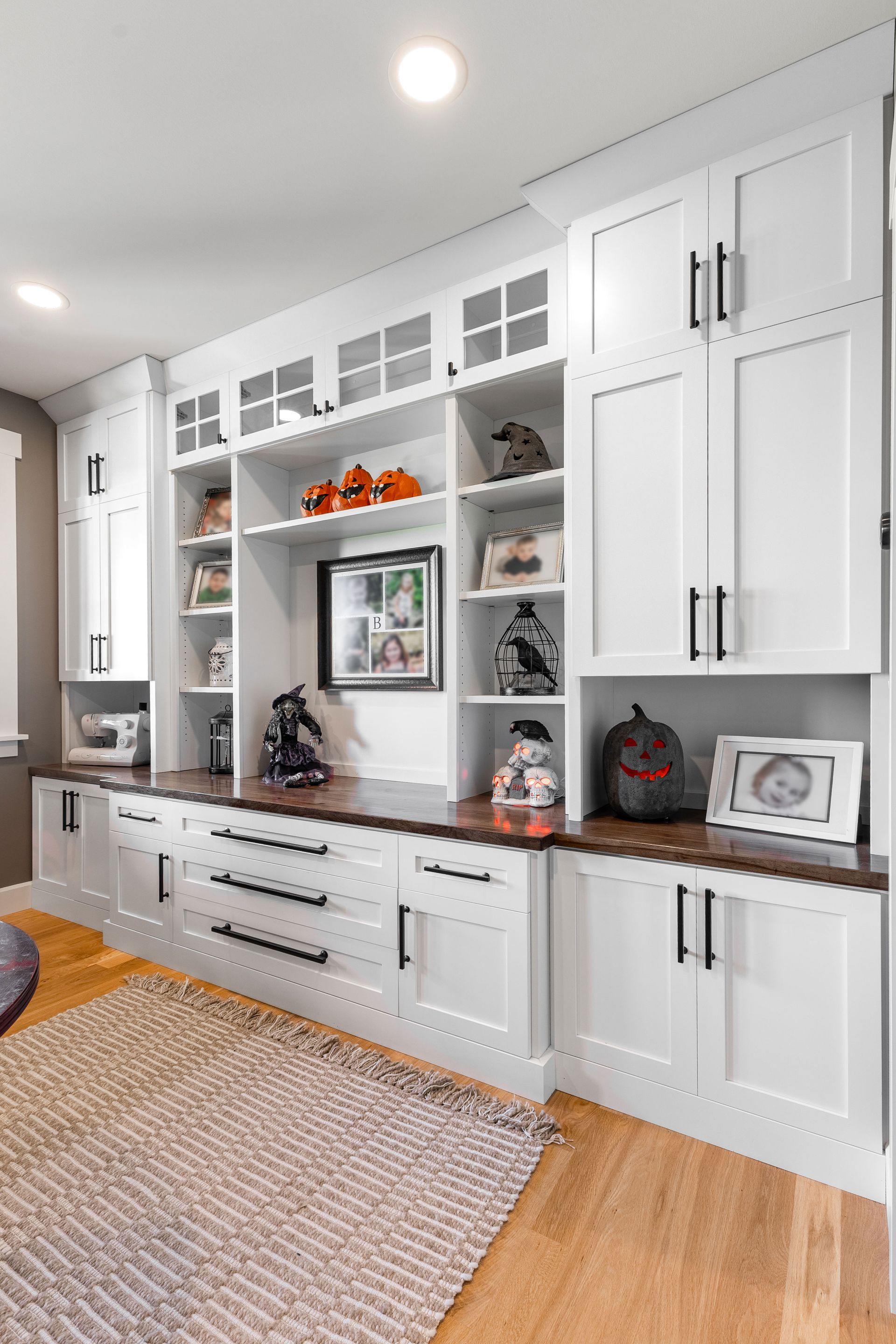 White built-in cabinet with open shelving and storage. Dark countertop, Halloween decorations, and rug on a hardwood floor.