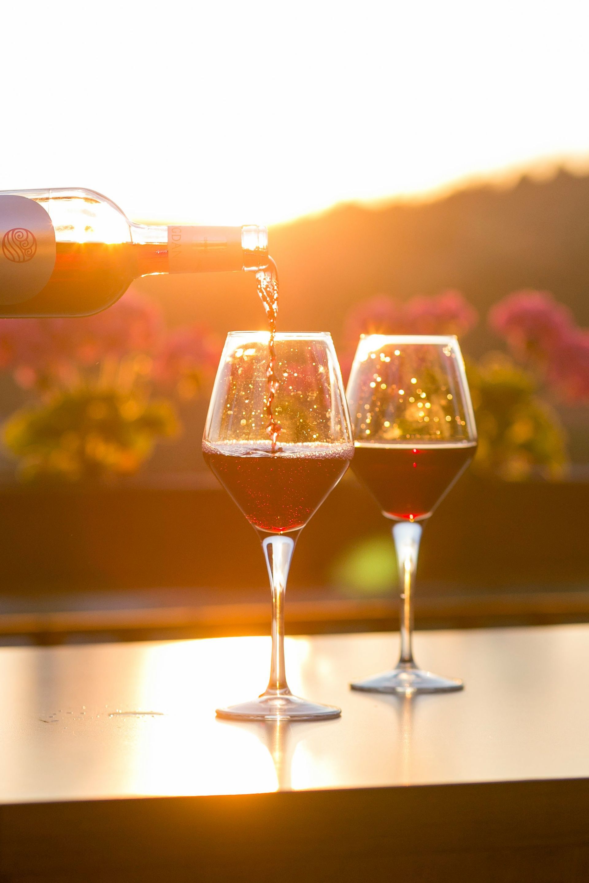 Red Wine is Being Poured Into One of Two Wine Glasses at Sunset — Mudgee Passenger Transport in Mudgee, NSW