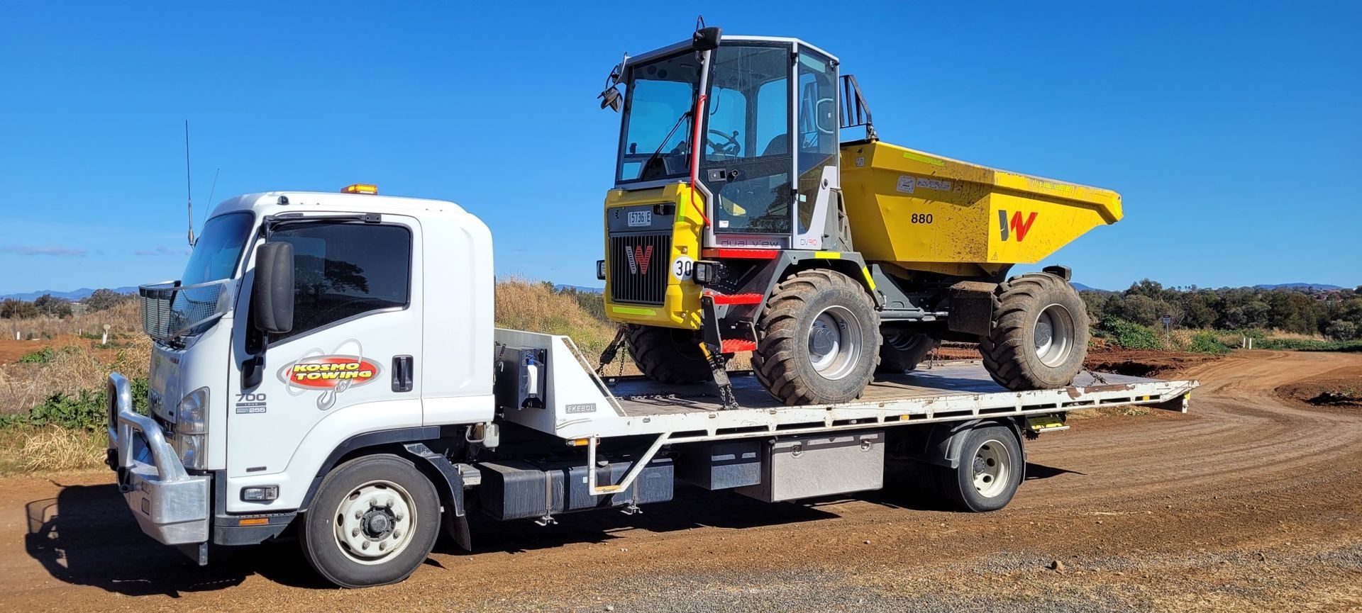A tow truck is carrying a dump truck on the back of it.