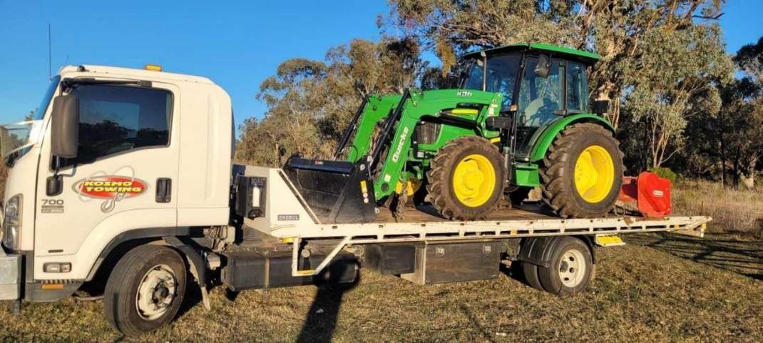 A tractor is being towed by a tow truck in a field.