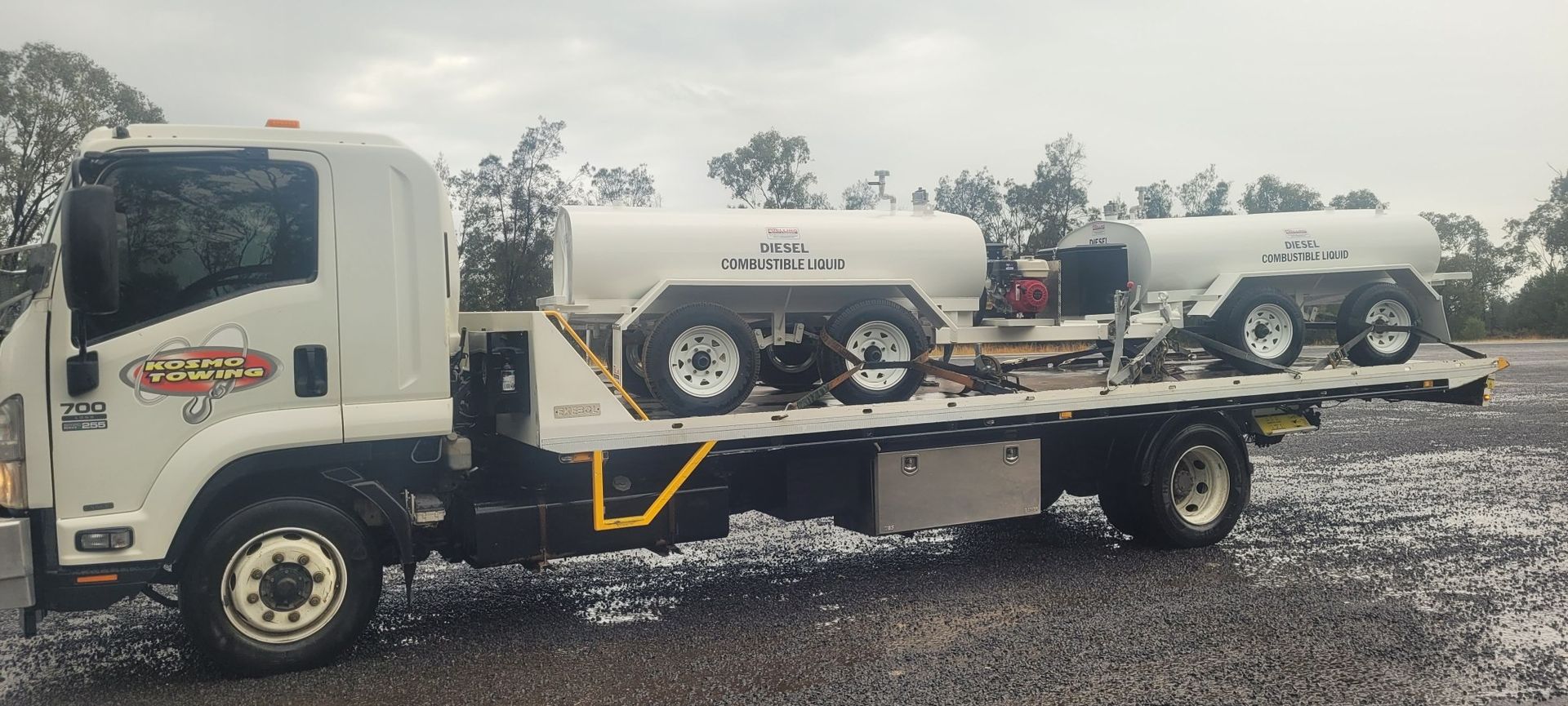 A white tow truck with two tanks on the back is parked in a gravel lot.