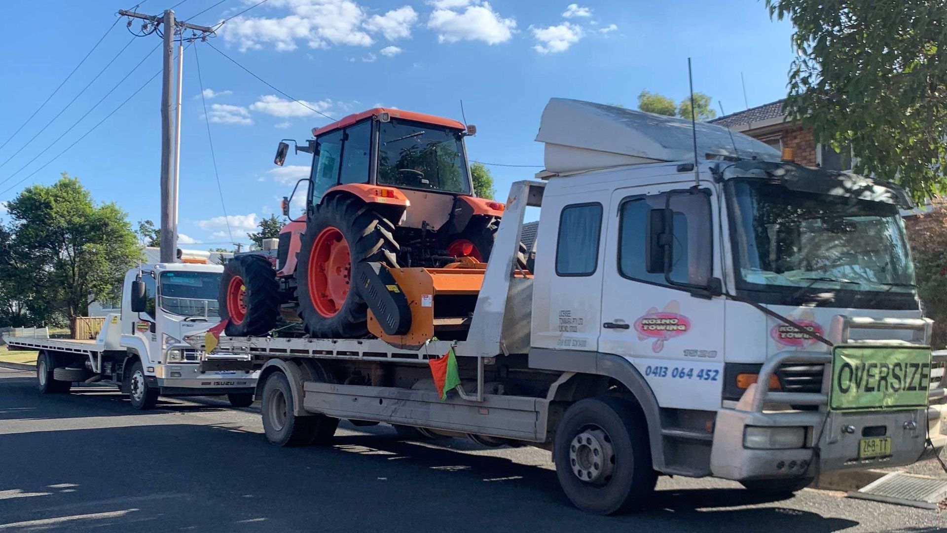 A tow truck is carrying a tractor on the back of it.