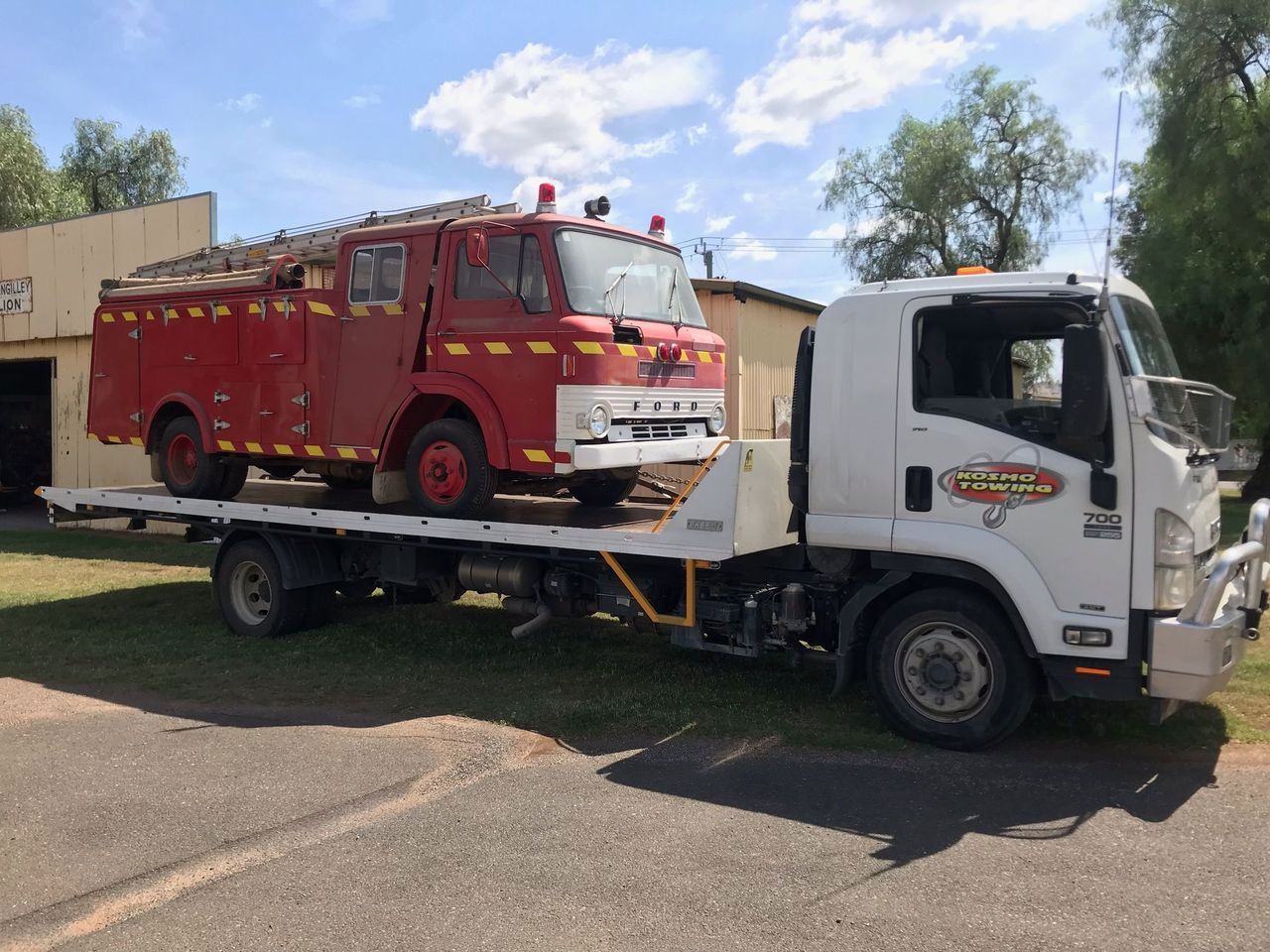A red fire truck is being towed by a white tow truck.
