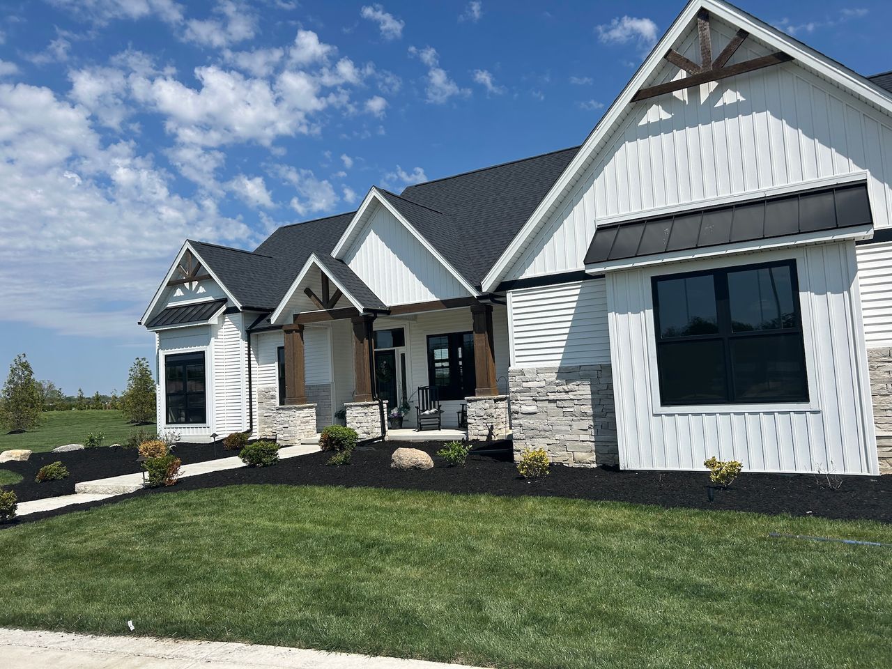 White house with black roof and trim, stone accents, and manicured landscaping under a blue sky.