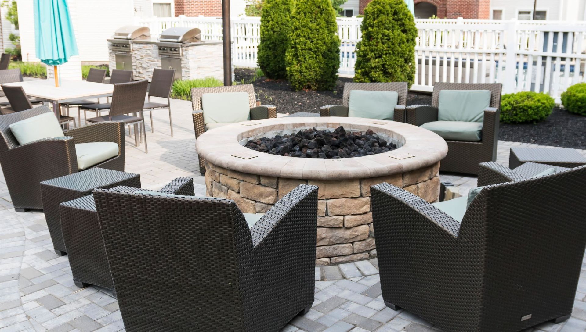 Patio with fire pit, seating, and green cushions.