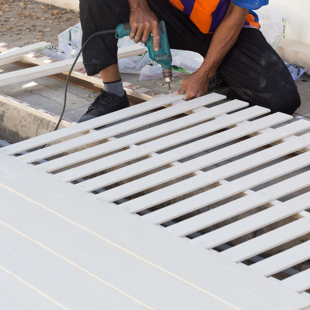 Person using a power drill on white wooden slats, outdoors.