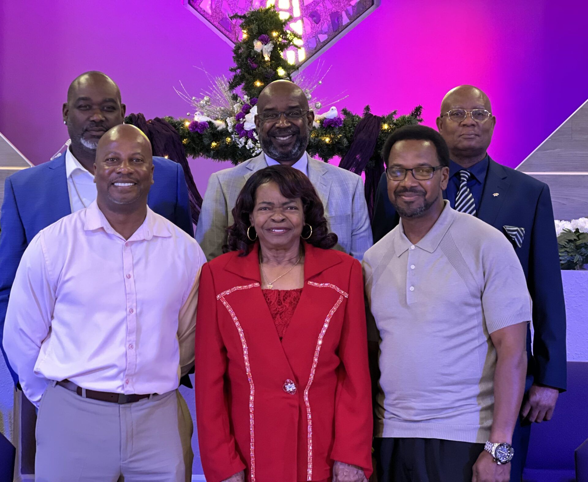 A group of six people stand smiling before a decorated altar in a church.