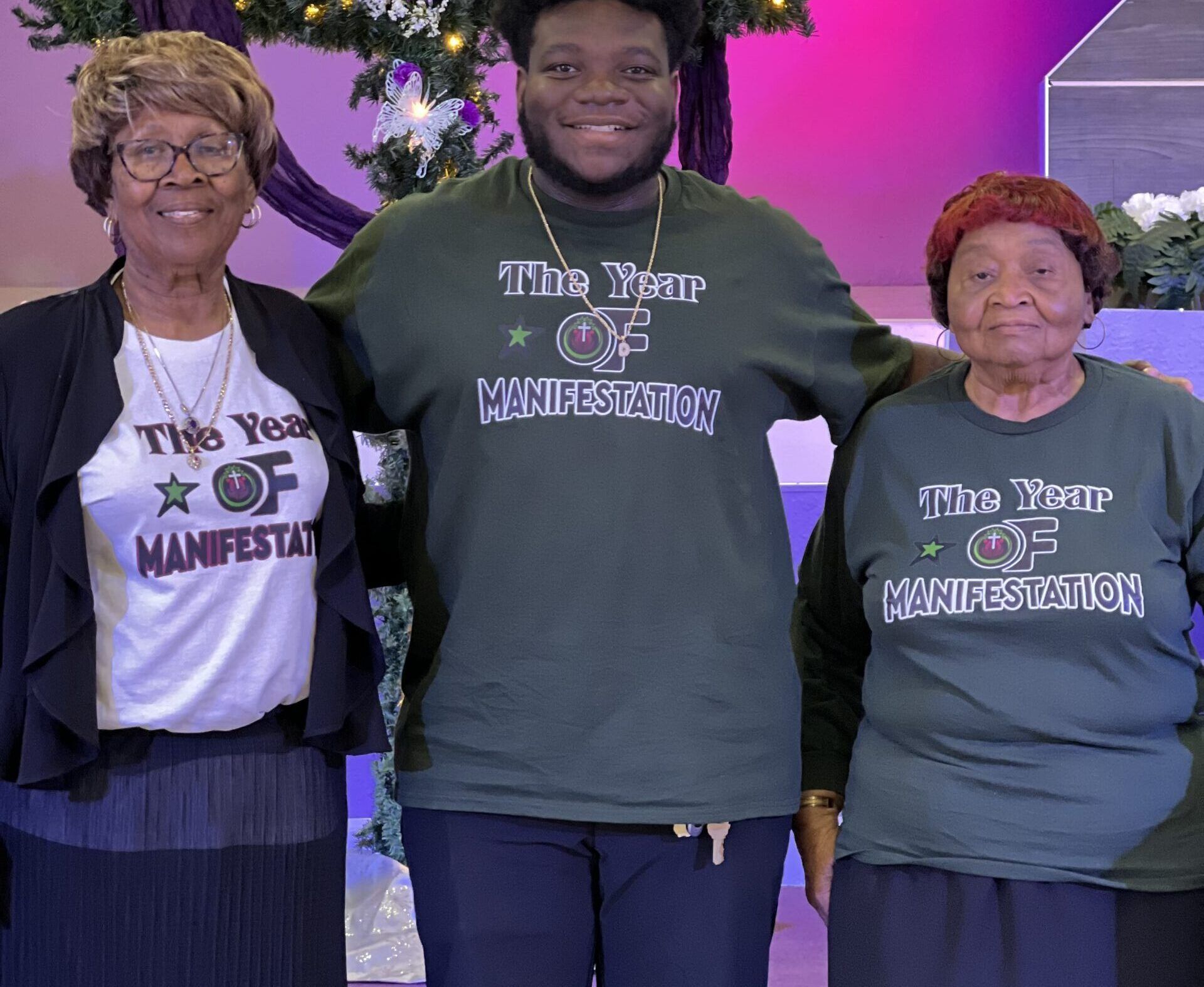Three people stand together, smiling, wearing matching shirts with the text 