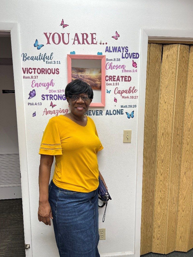 A person wearing a yellow top and denim skirt stands in front of a wall featuring inspirational text and butterflies.