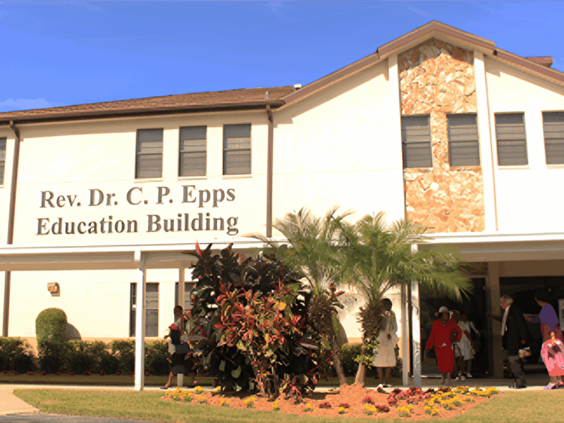 The Rev. Dr. C. P. Epps Education Building with people walking into the entrance under a covered walkway on a sunny day.