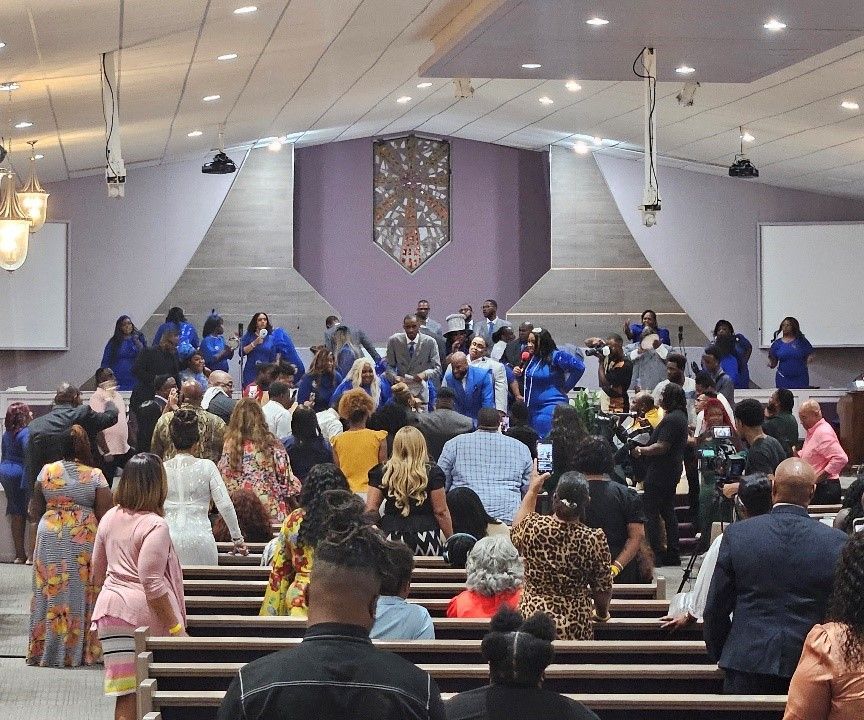 A large group of people gather in a church sanctuary, with many standing and interacting among the pews.