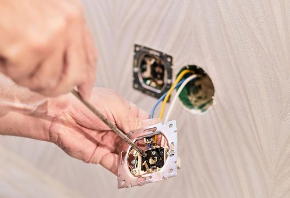 Hands wiring a white electrical wall outlet box in a wall cutout