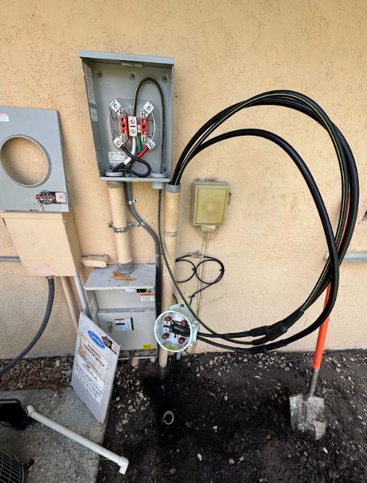 Electrical service boxes and coiled black cable on a stucco wall next to a small gray utility cabinet.