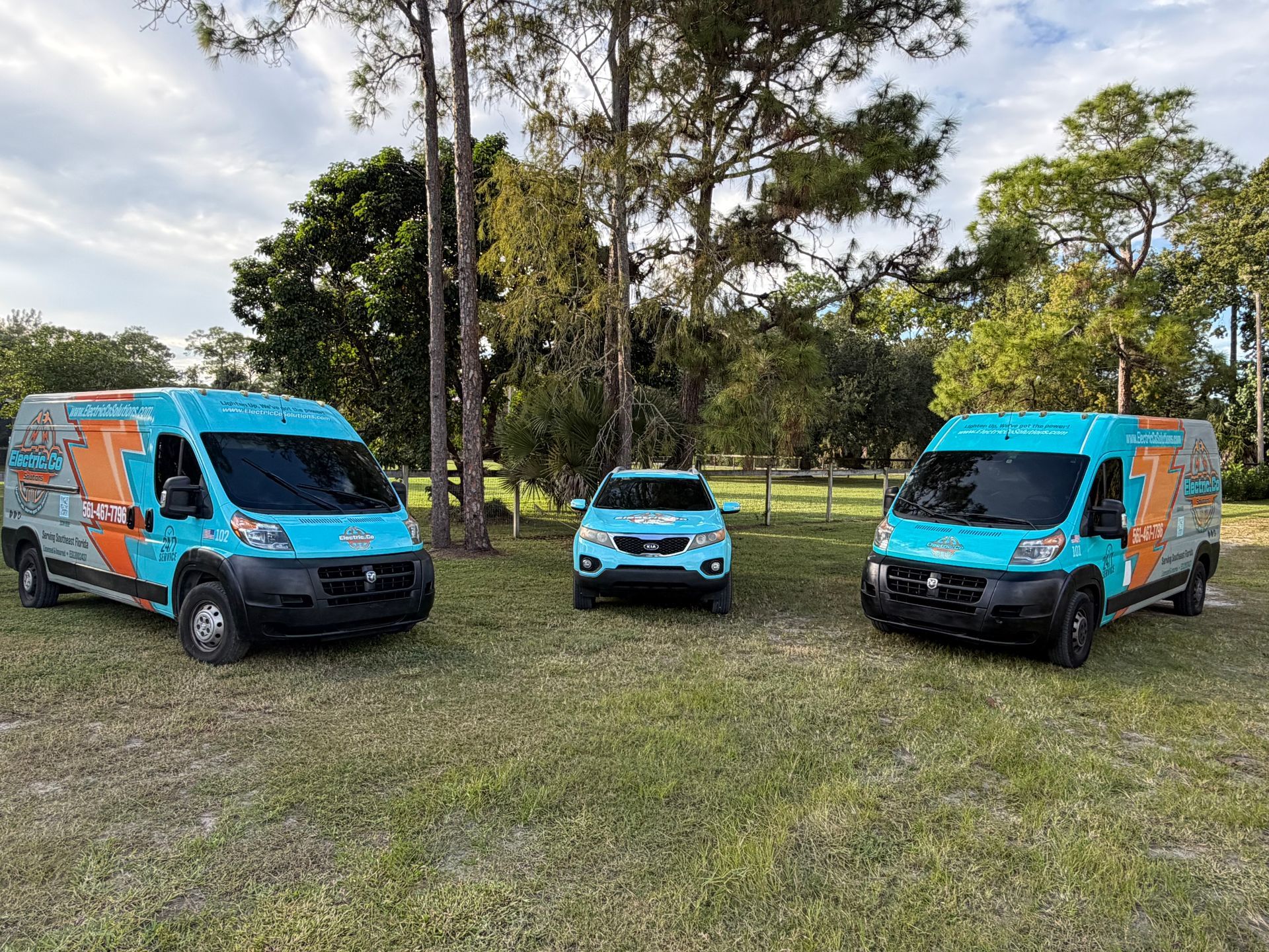 Three bright blue and orange vans parked on grass in a park-like field