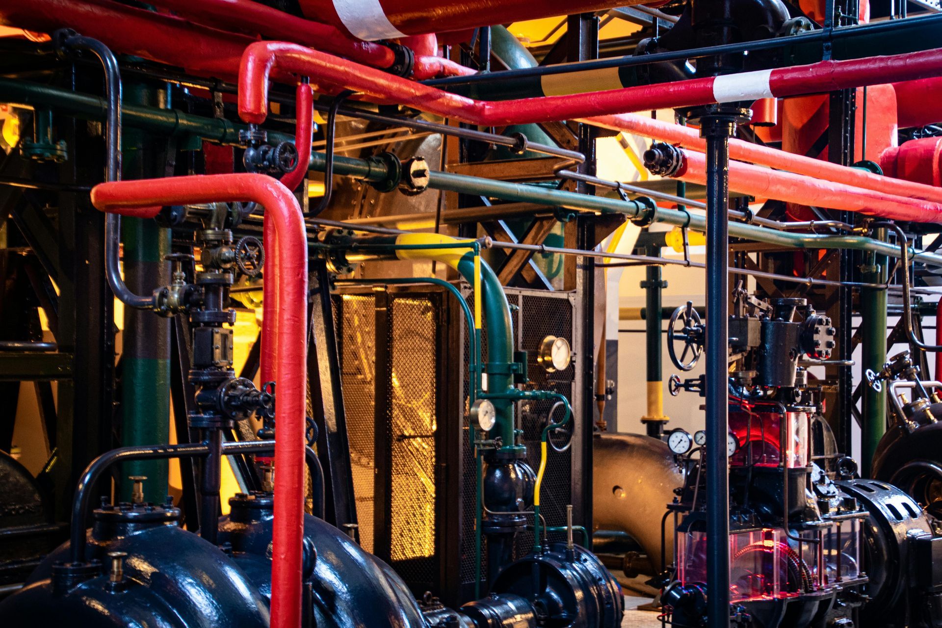 Red and green pipes in an industrial setting, with machinery and gauges, dark background. Phoenix Plumbing Co.