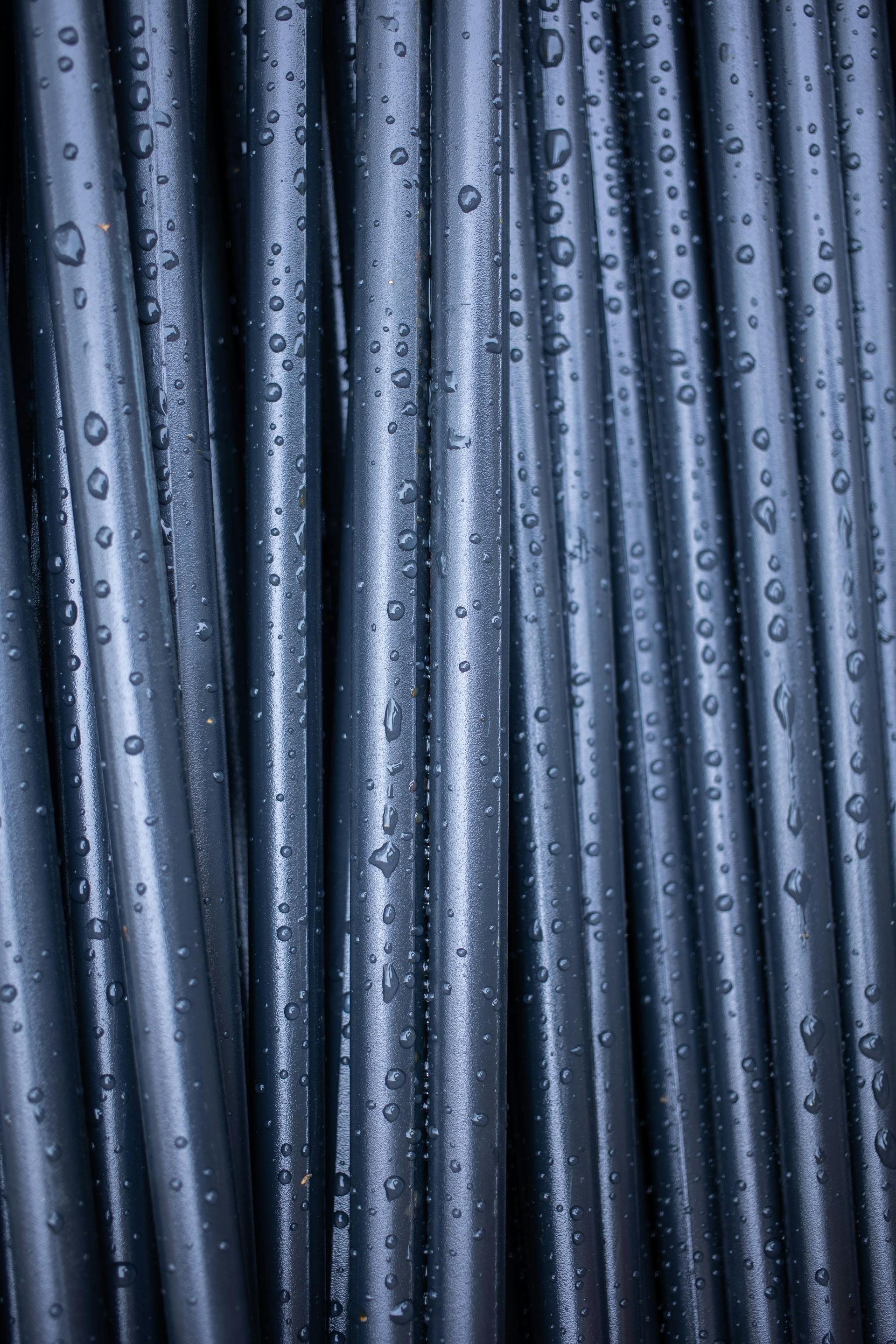 Close-up of wet, silvery-blue cylindrical tubes arranged vertically, covered in water droplets. Phoenix Plumbing Co.
