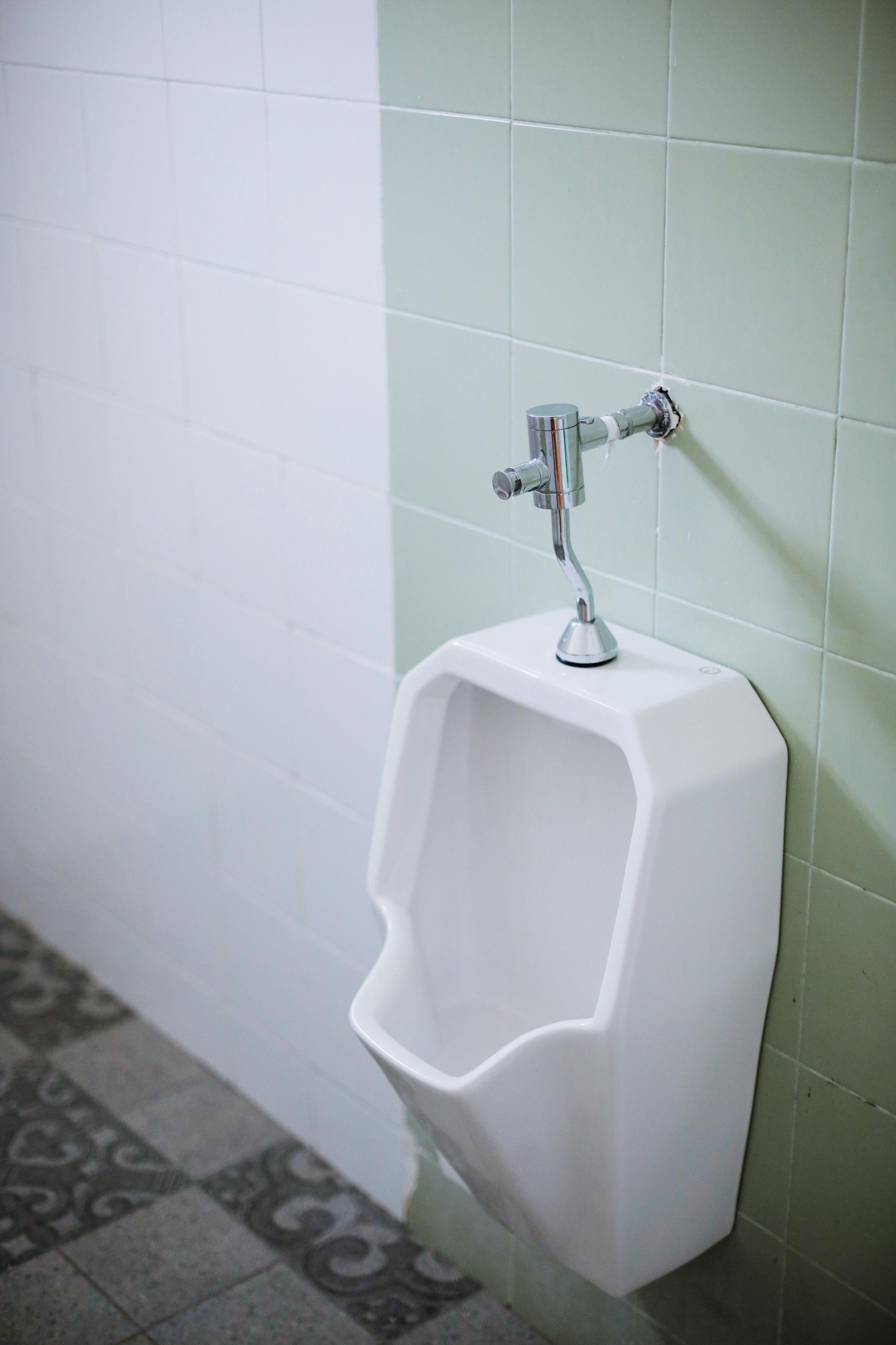 White urinal in a public restroom with light green and white tile walls.