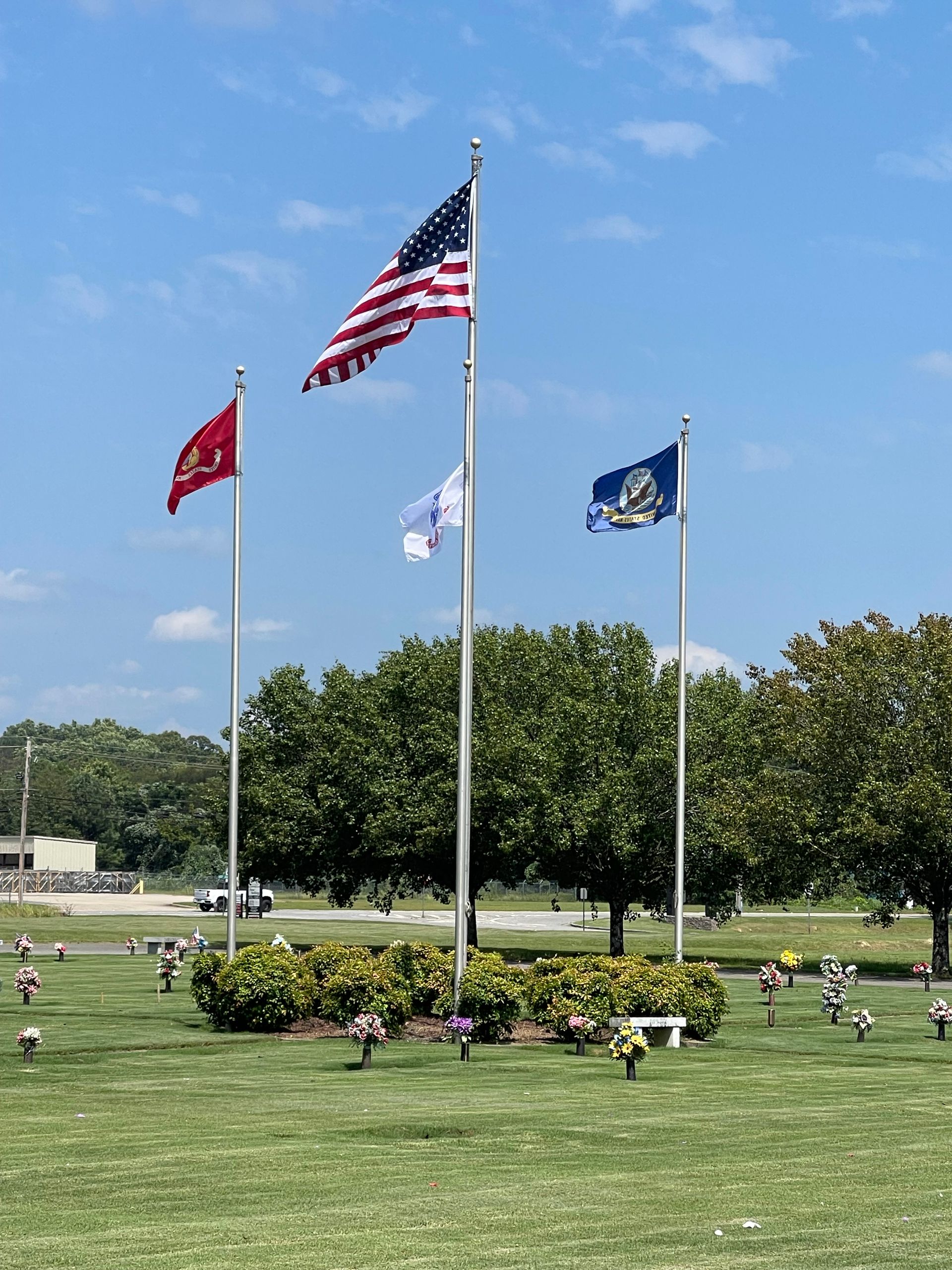 Three flags are flying in a cemetery on a sunny day.