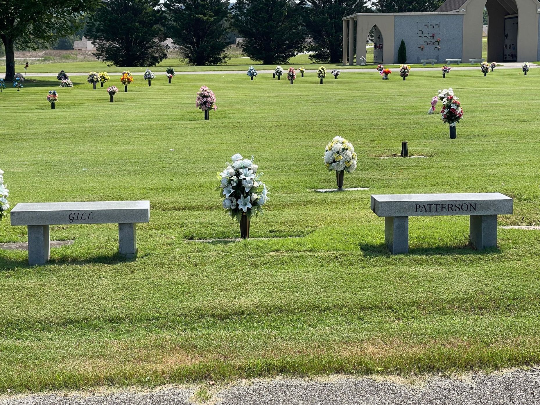 A cemetery with two benches and flowers in the grass