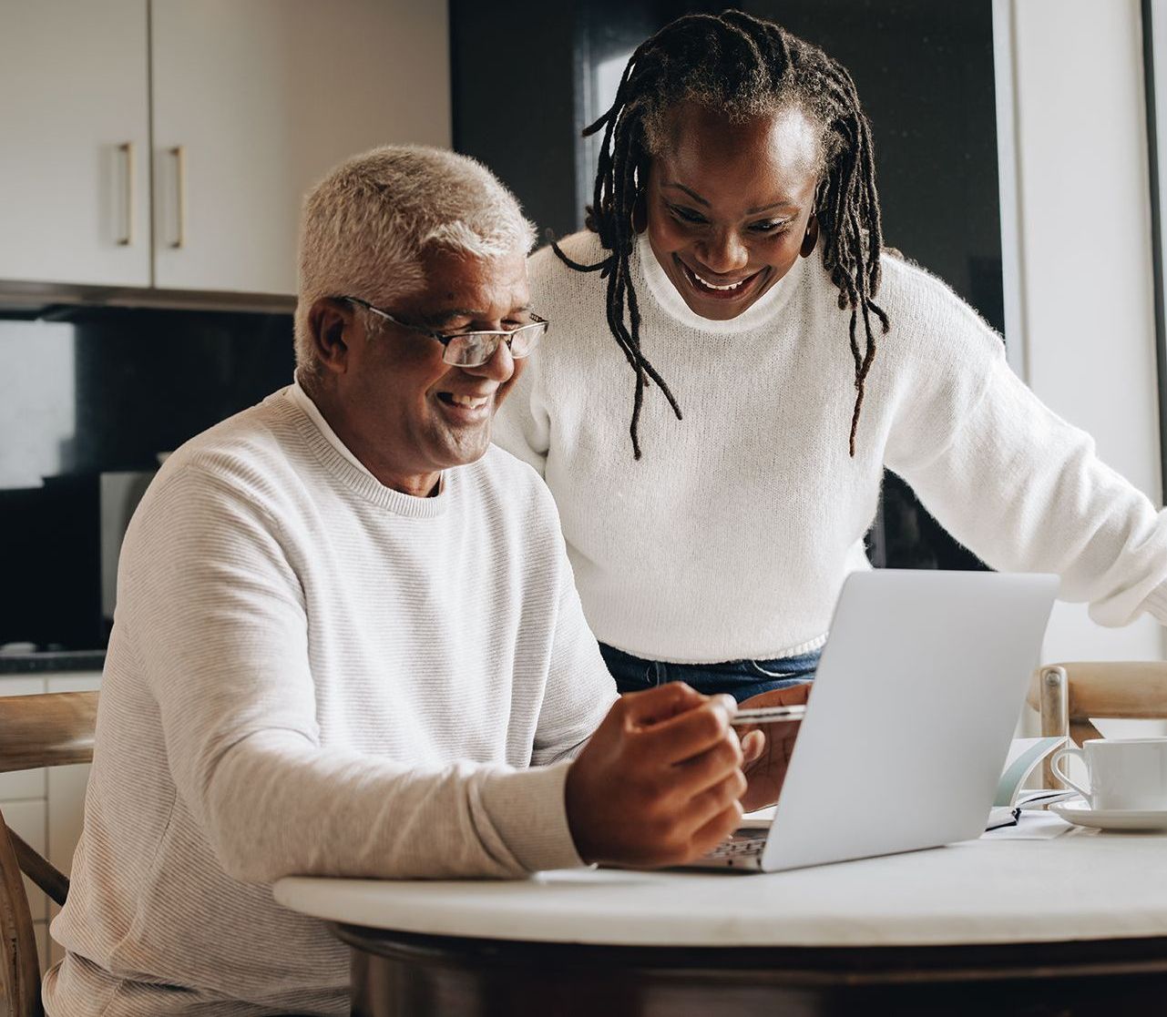 A man and a woman are sitting at a table looking at a laptop computer.