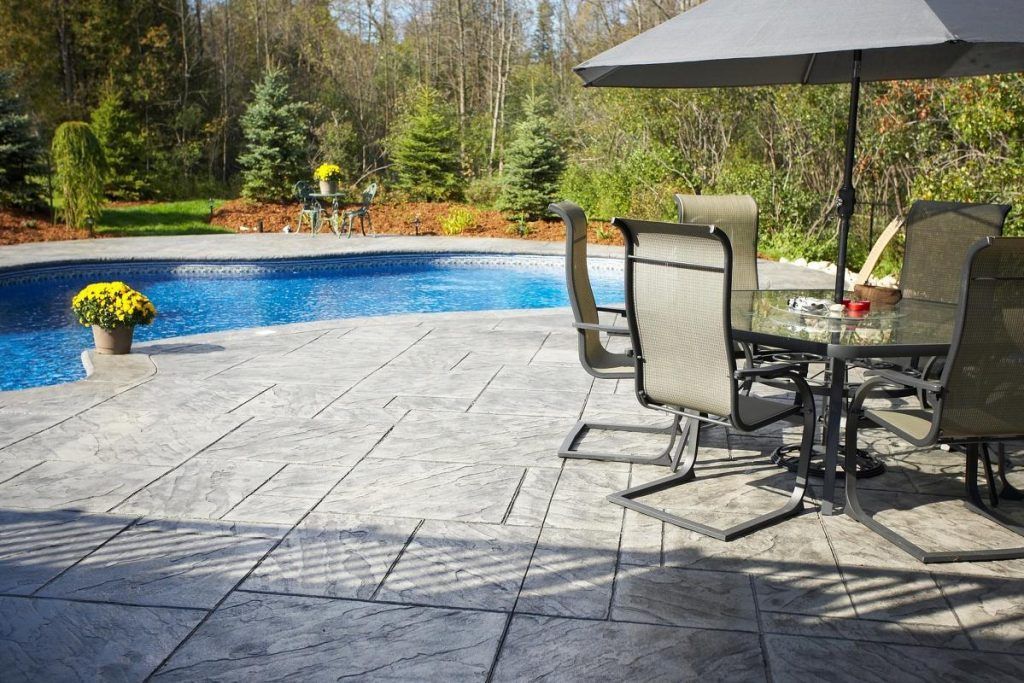 A patio with a table and chairs and an umbrella next to a pool.