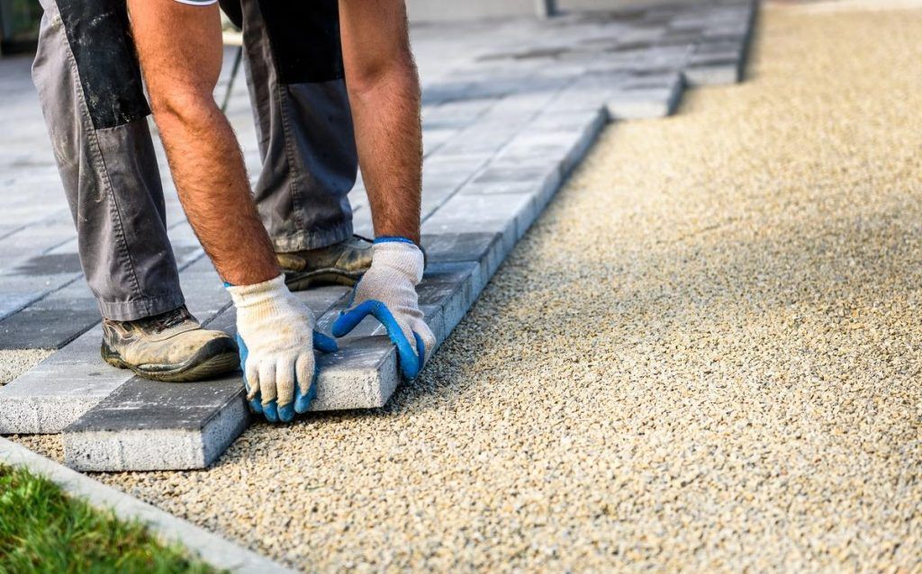 A man is laying bricks on a sidewalk.