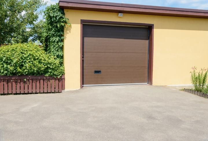 A yellow garage with a brown garage door and a driveway.