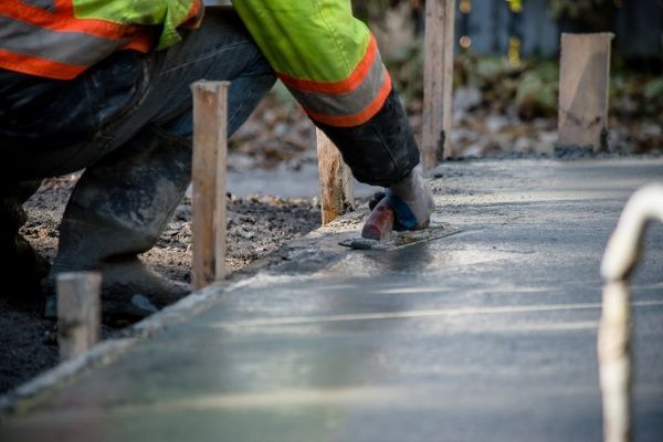 A construction worker is spreading concrete on a sidewalk.