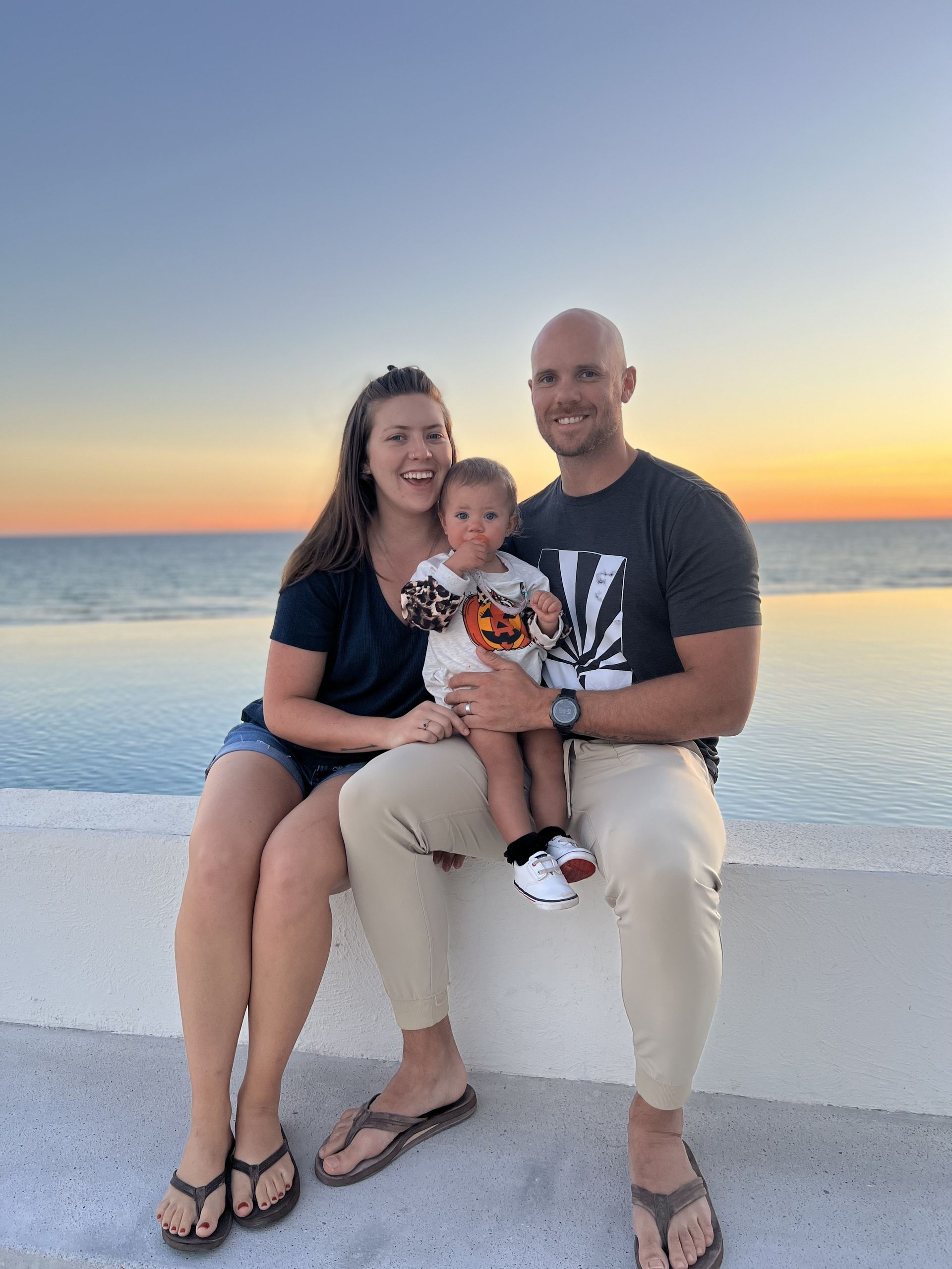 A man and a woman are sitting on a wall holding a baby.