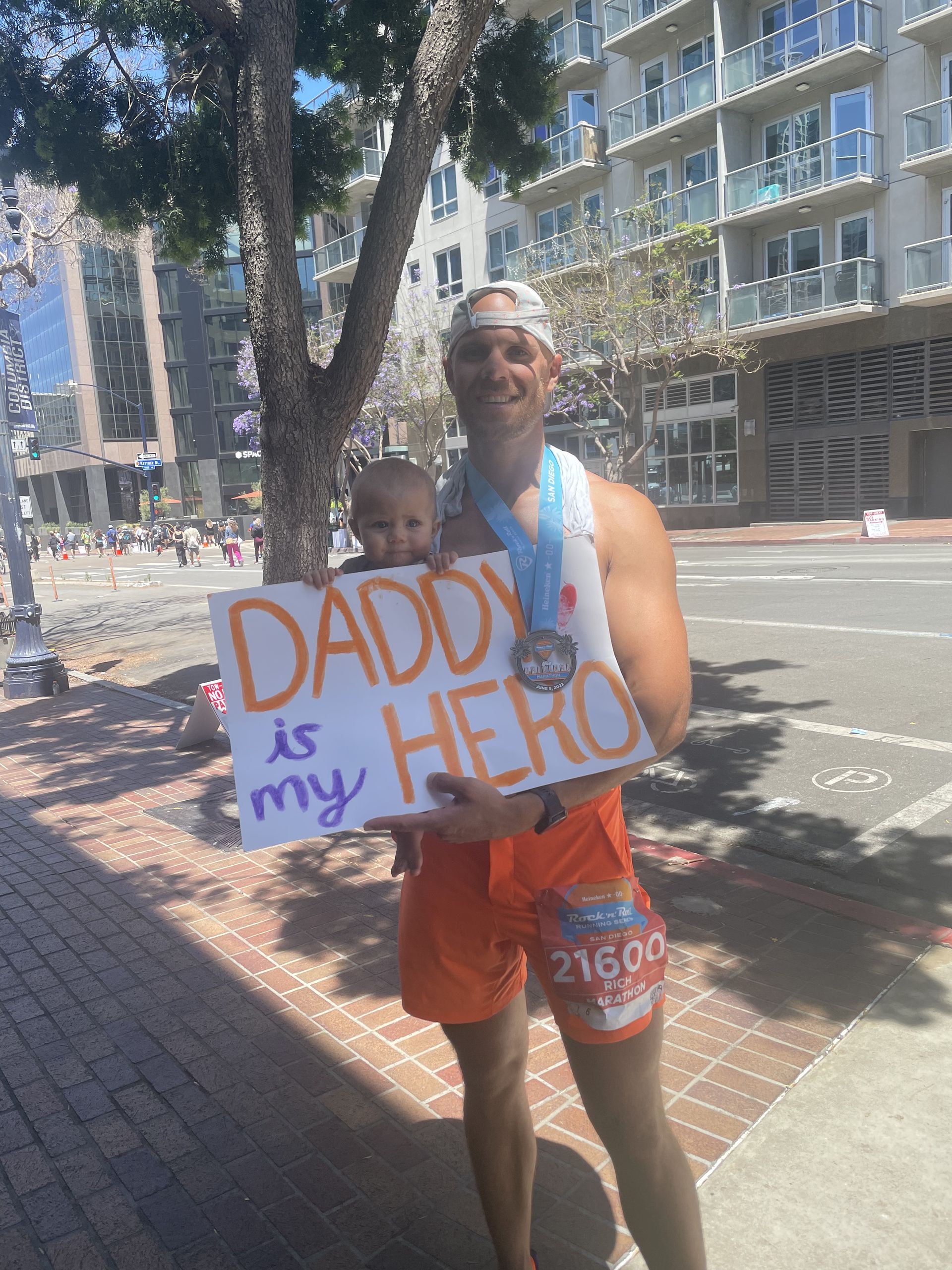 A man is holding a baby and holding a sign that says daddy is my hero