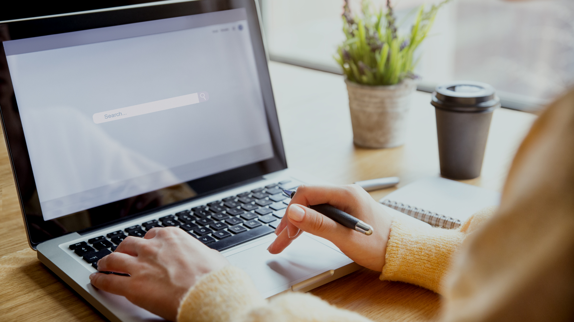 A person is typing on a laptop computer while holding a pen.
