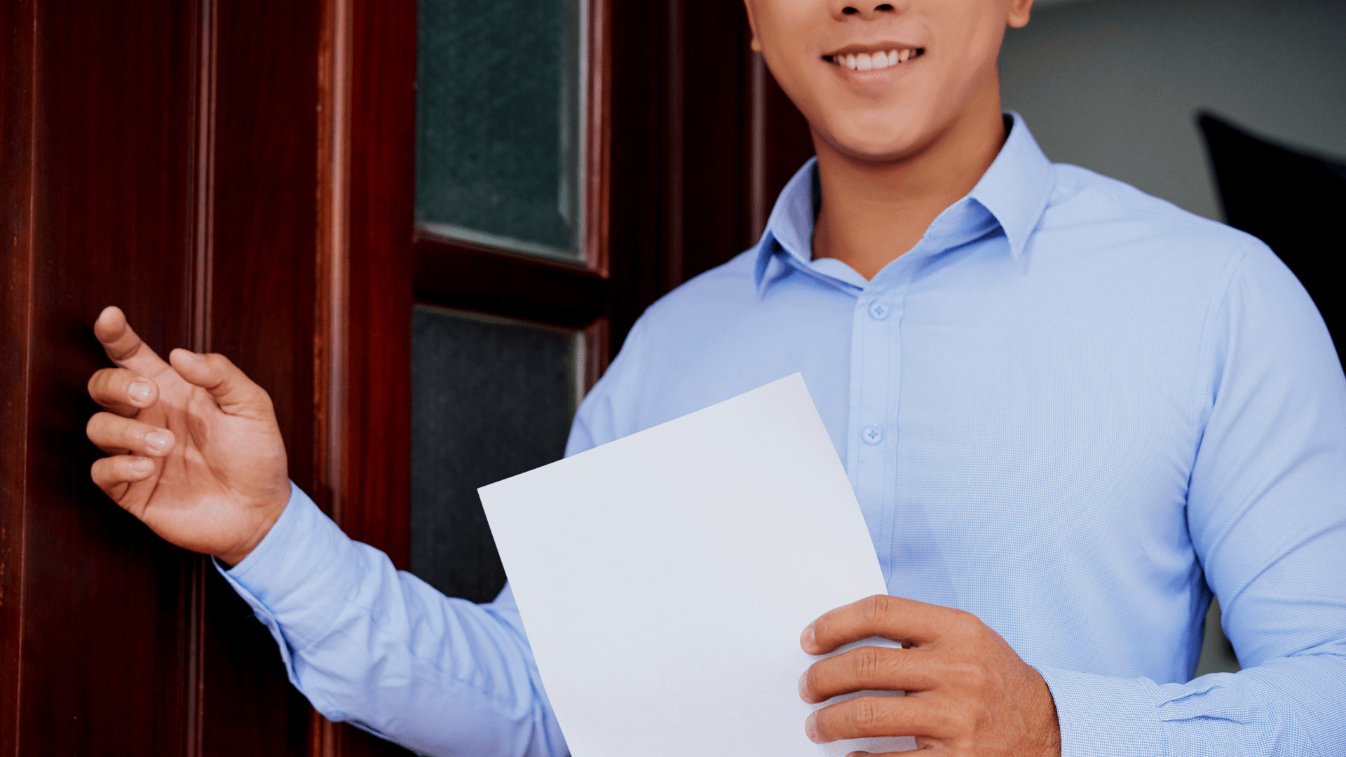 A man in a blue shirt is holding a piece of paper in front of a door.