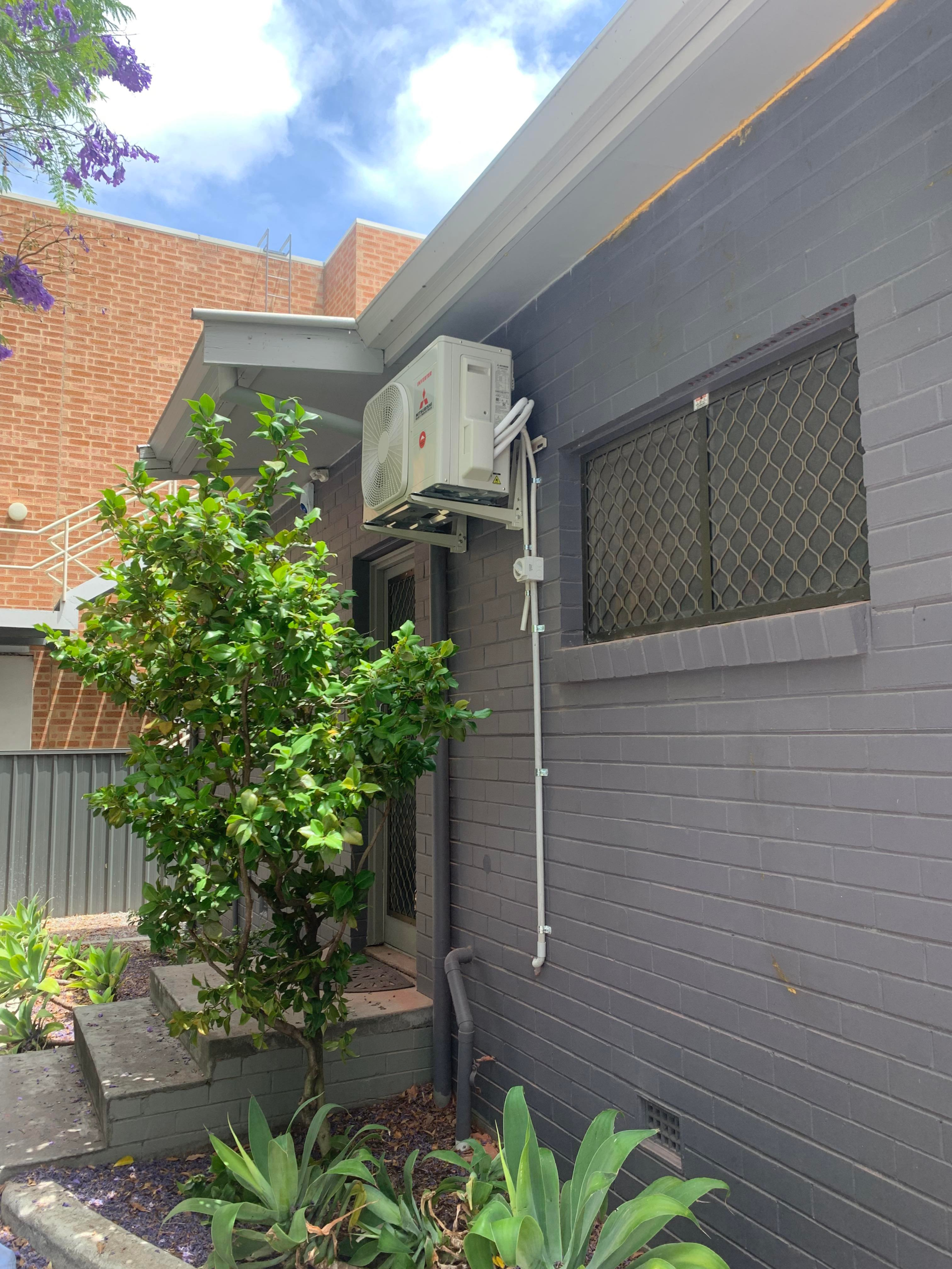 Mitsubishi split system wall mounted onto the side f a house to cool living room