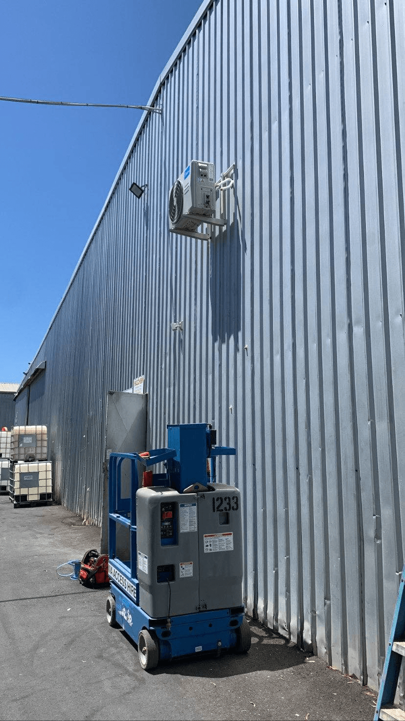 Split system mounted on the side of a workshop shed using a scissor lift to reach it in  Wangara Perth WA