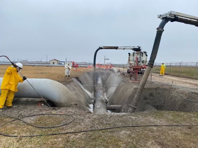 A man in a yellow suit is cleaning a pipe with a hose.