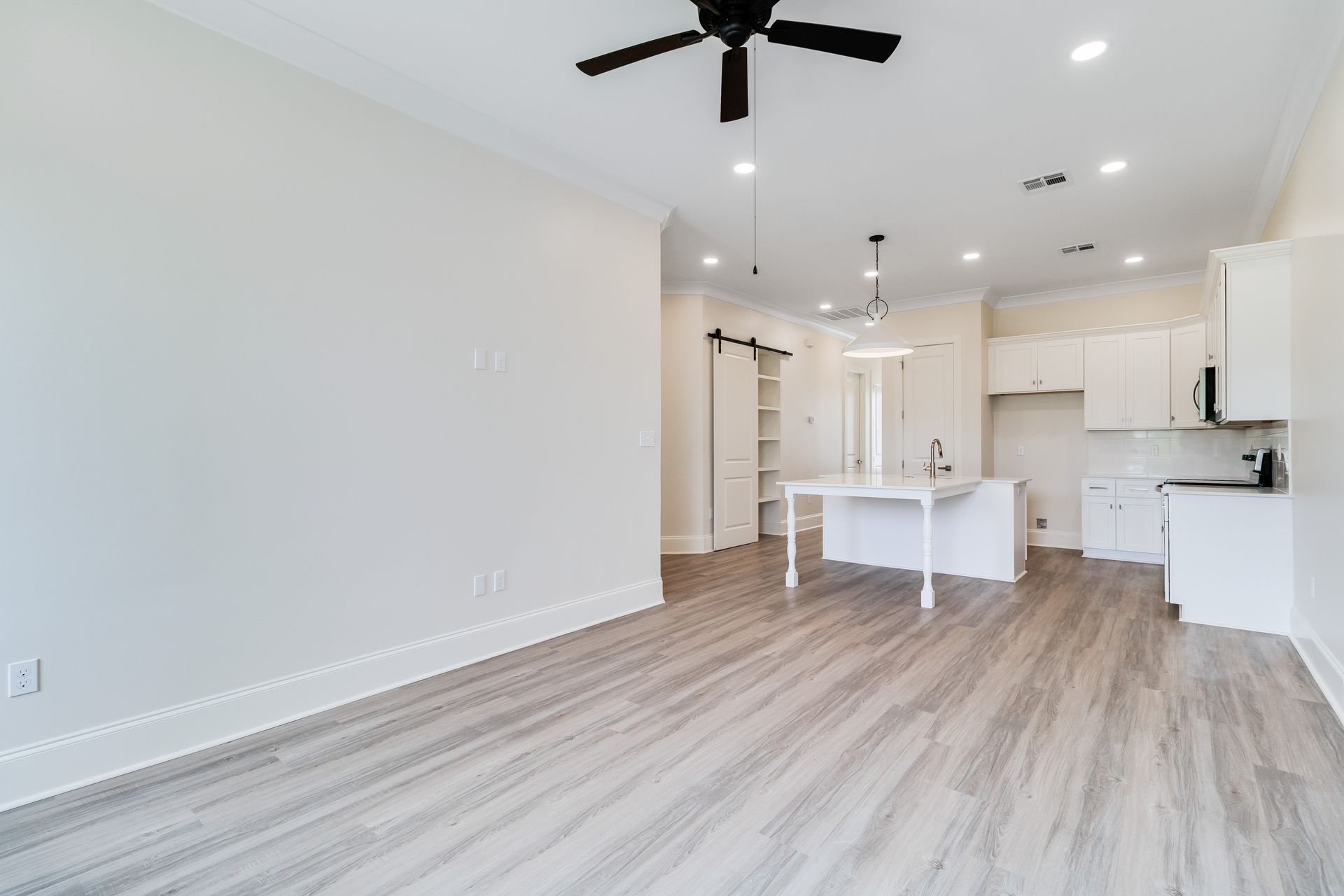 There is a ceiling fan in the living room and a kitchen in the background.