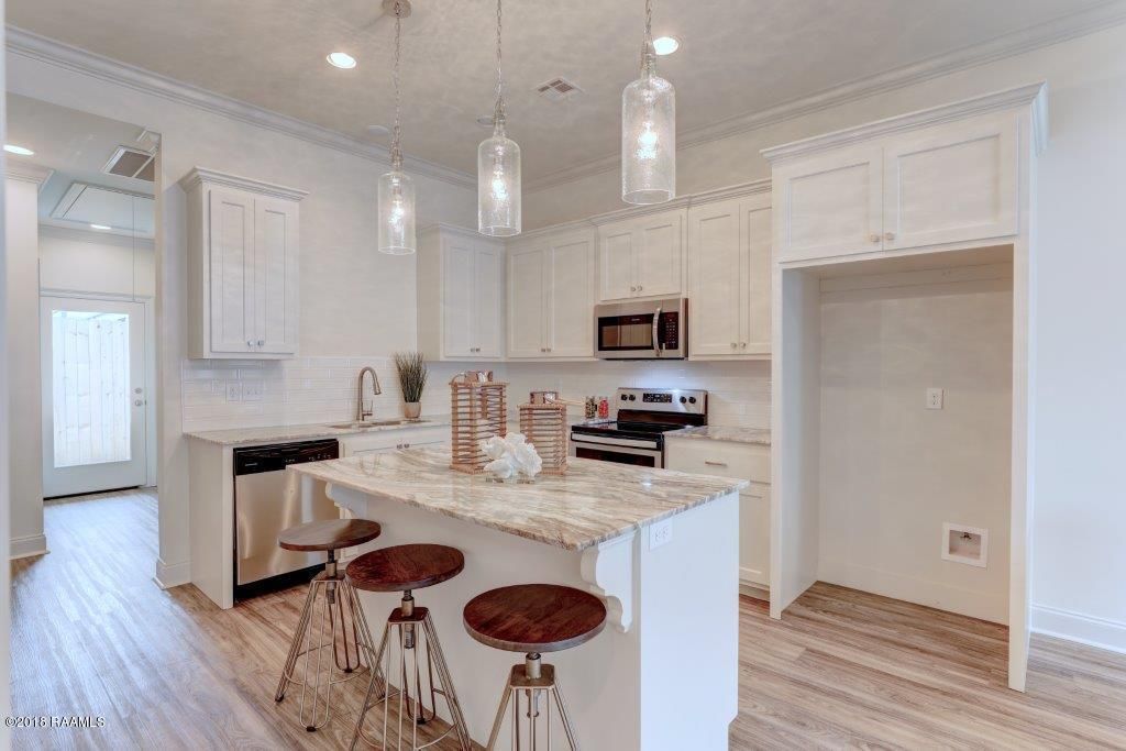 A kitchen with white cabinets , granite counter tops , stainless steel appliances and a large island.