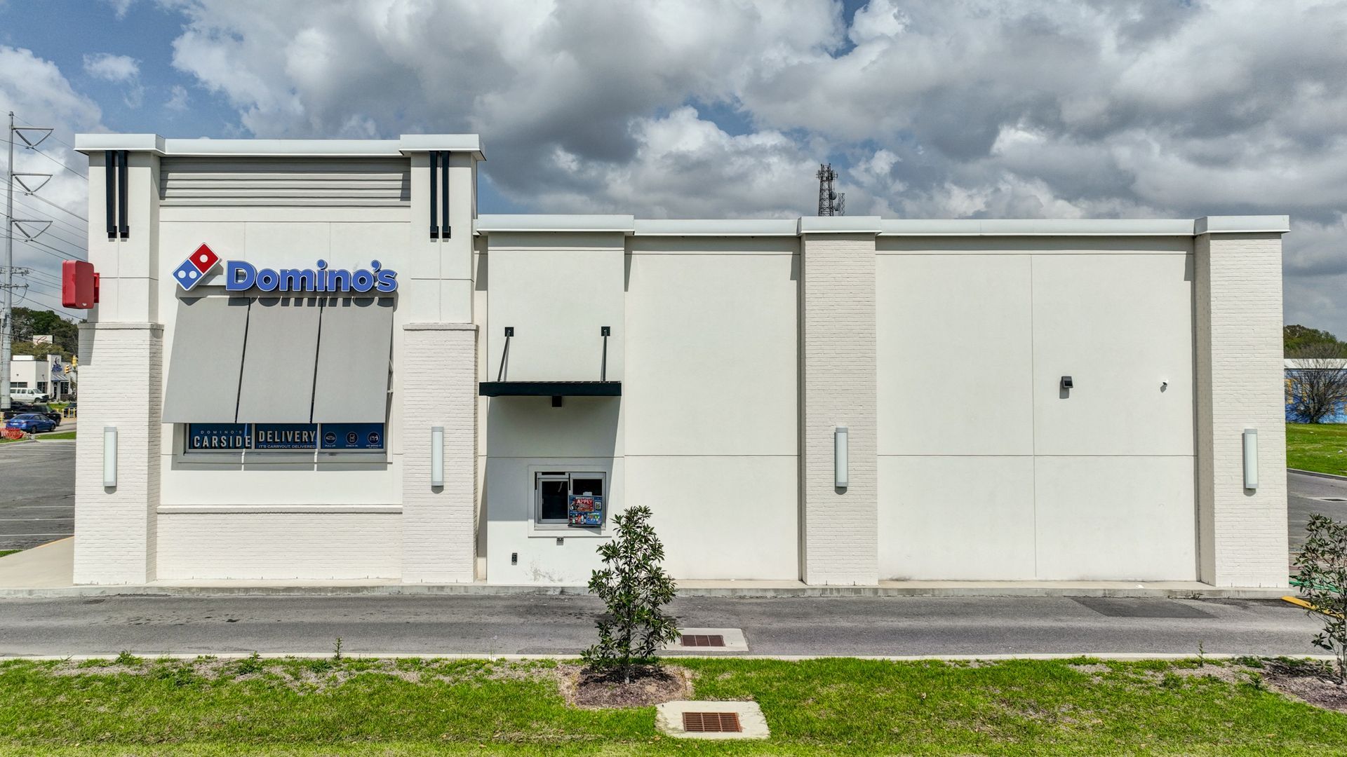 A domino 's pizza restaurant is sitting in the middle of a grassy field.